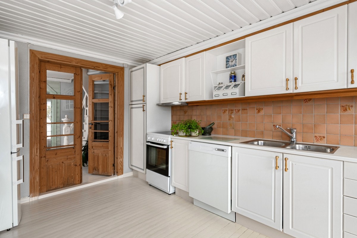 Kjøkkeninnredningen er plassert langs den ene veggen og består av over- og benkeskap med profilerte, hvite fronter. Galleribilde