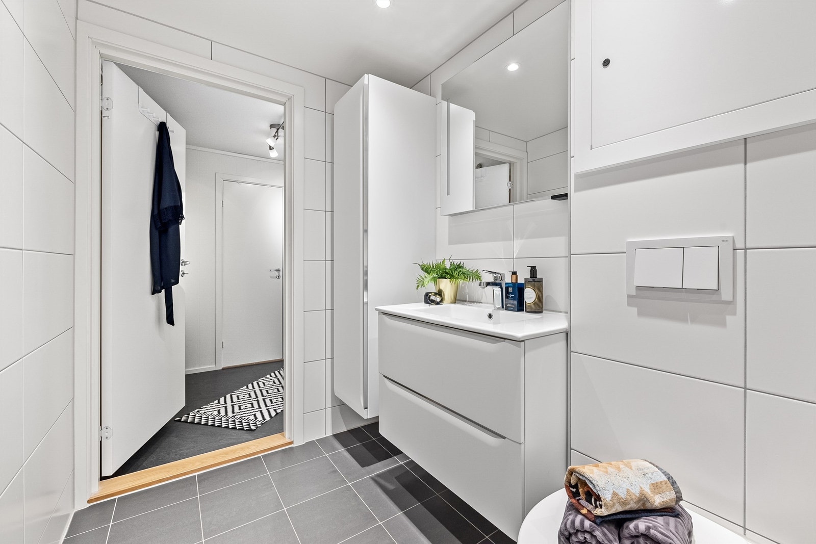 Badet har varmekabler i gulv og inneholder servantskap med slette fronter, speil på vegg, veggehengt toalett, samt dusjhørne med innfellbare glassdører. Det er i tillegg opplegg for vaskemaskin og tørketrommel. Galleribilde