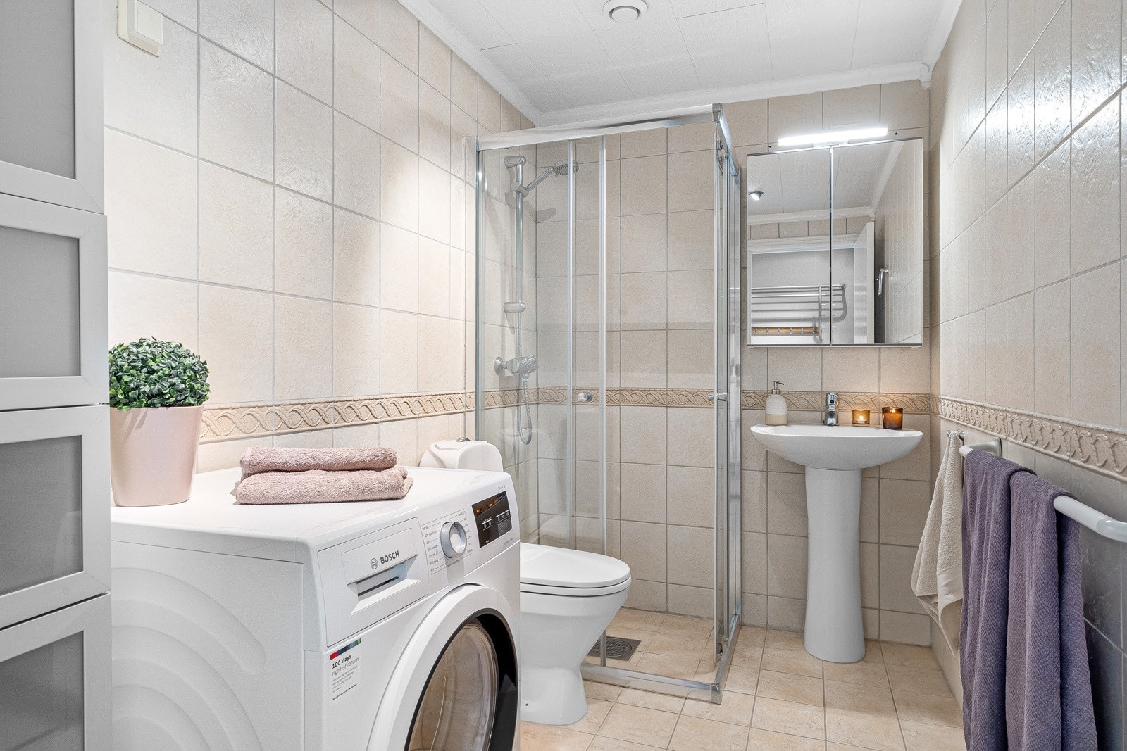 Flott flislagt bad med varmekabler i gulv, downlights i himling og opplegg for vaskemaskin Galleribilde