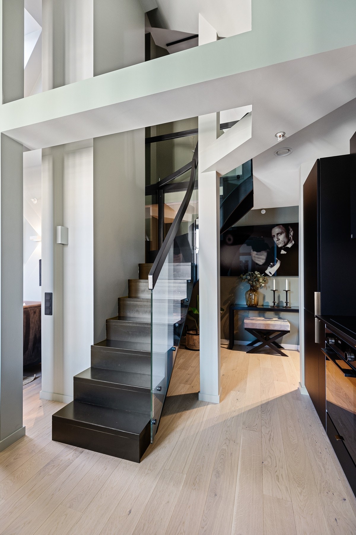 Fra kjøkkenet er det en mørkbeiset trapp med glassrekkverk opp til mesaninen. Galleribilde