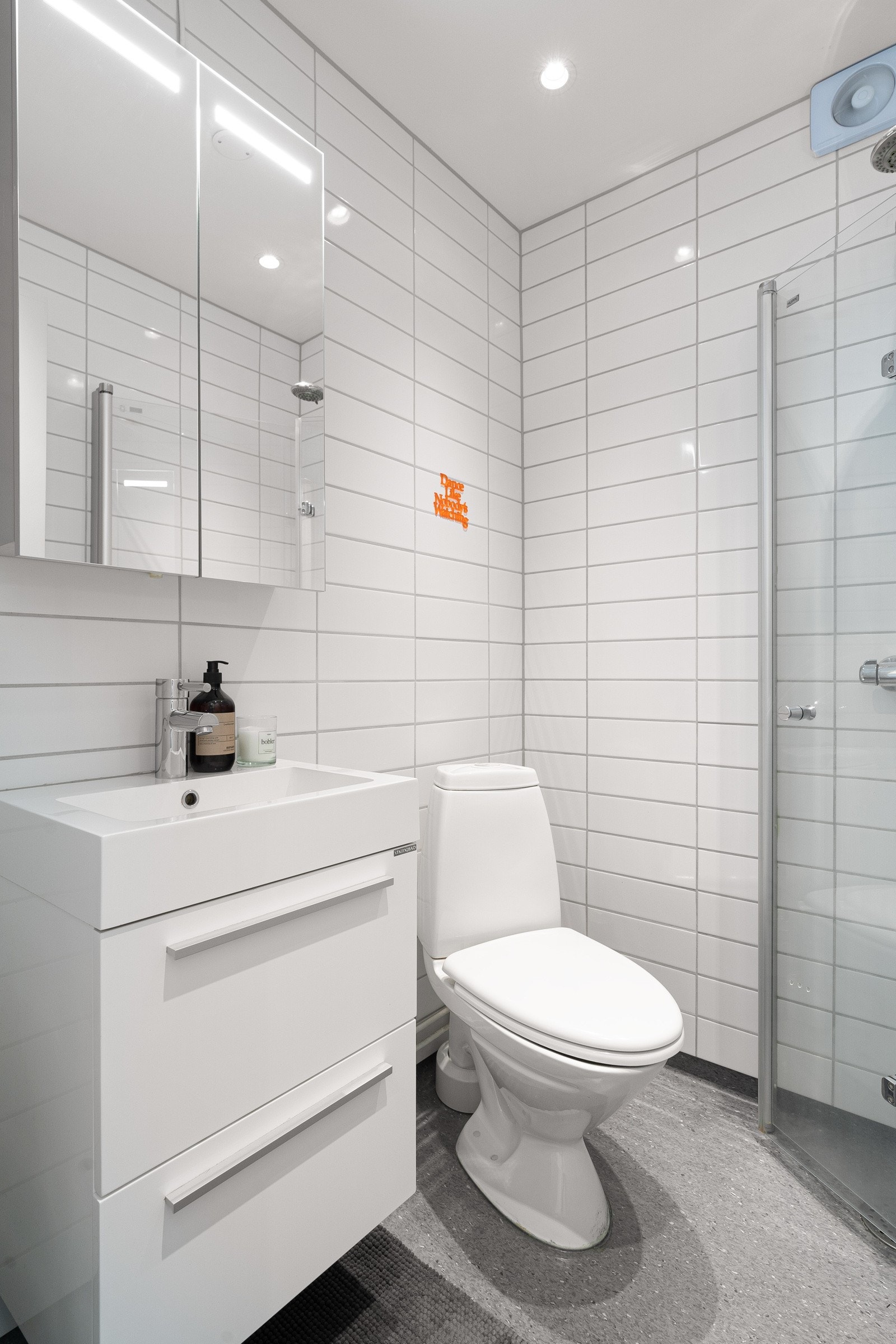 Baderom med servant- og speilskap, gulvmontert toalett og dusjnisje med glassdører Galleribilde