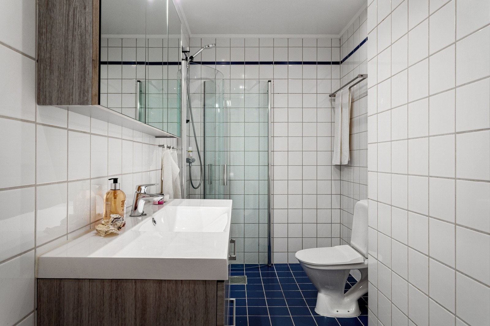 Baderommet har mørke fliser på gulv med gulvvarme, hvite fliser på veggene og downlights i himlingen. Galleribilde
