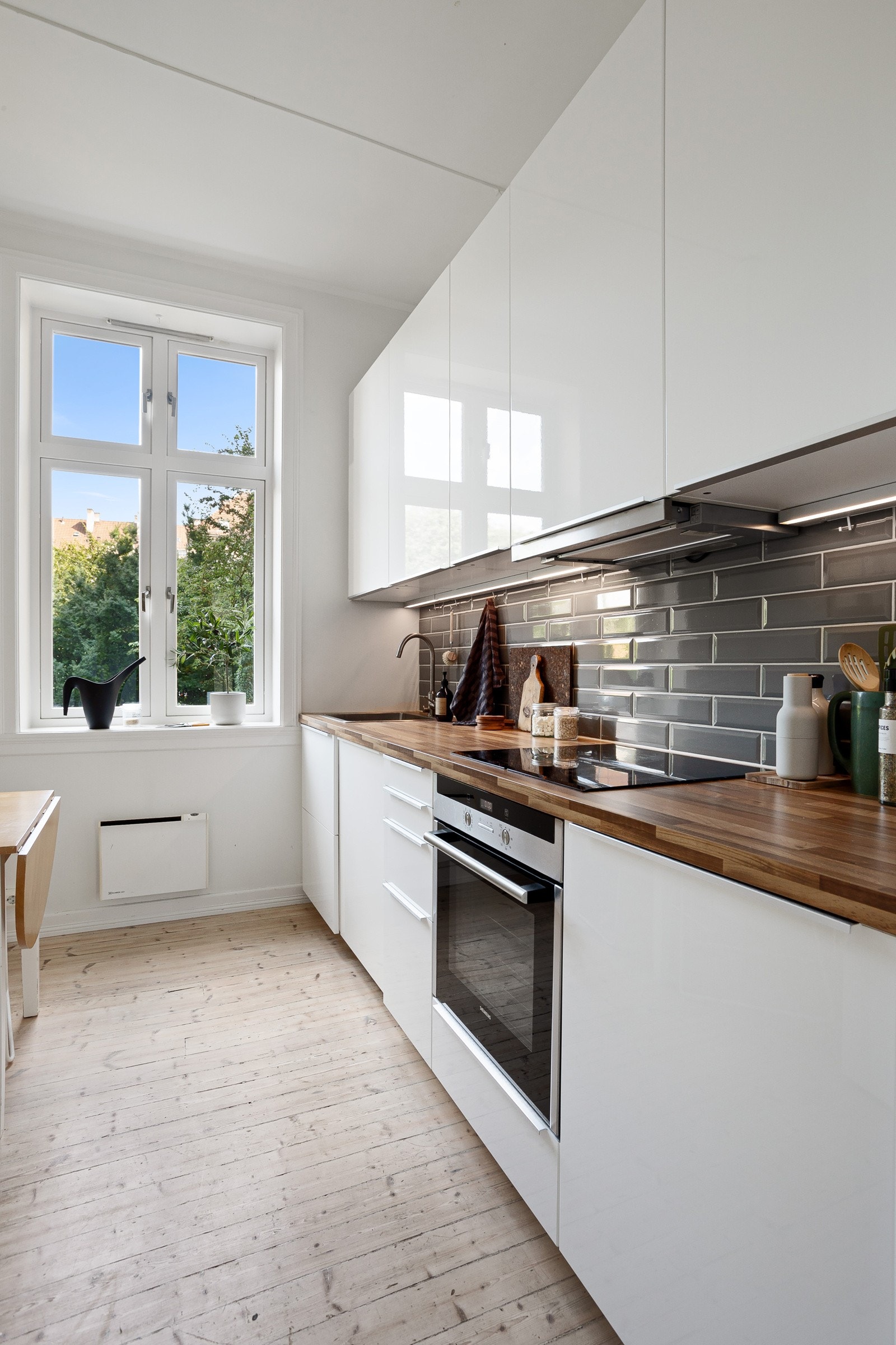 Moderne og tidløs kjøkkeninnredning med hvite glatte fronter og laminert benkeplate med nedfelt oppvaskkum. Praktisk med lekre fliser i benkeryggen og belysning under overskapene. Galleribilde