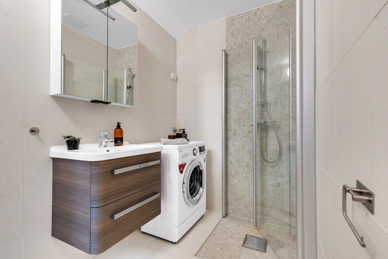 Lekkert, flislagt bad med svingbare dusjdører i herdet glass, servant med servantskap, speil og vegghengt klosett. Galleribilde