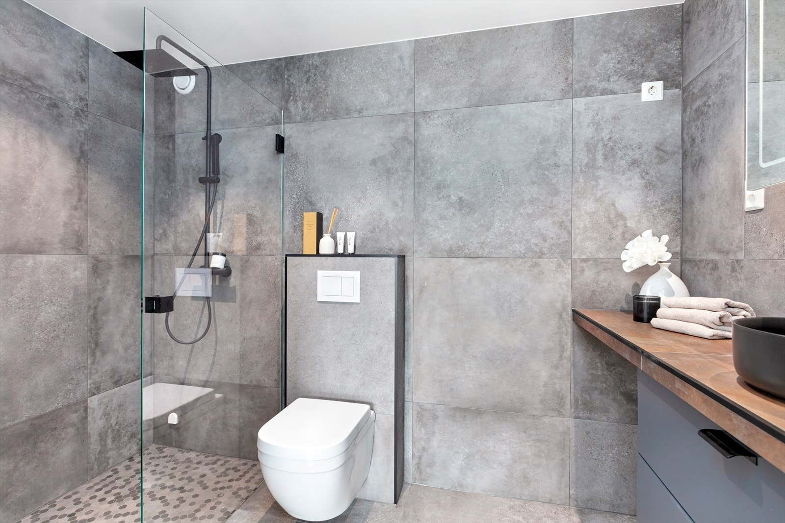 Badet har vegghengt wc, servantskap med underskap, toppmontert servant og speilskap. Dusjsonen er skjermet med en stor glassvegg med mosaikkfliser på gulvet. Galleribilde
