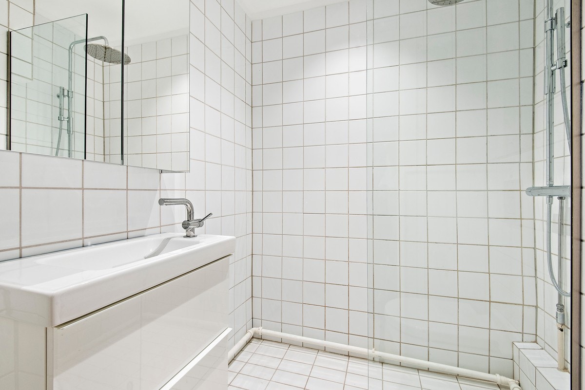 Lyst baderom med dusjhjørne, vegghengt toalett og opplegg for vaskemaskin. Galleribilde