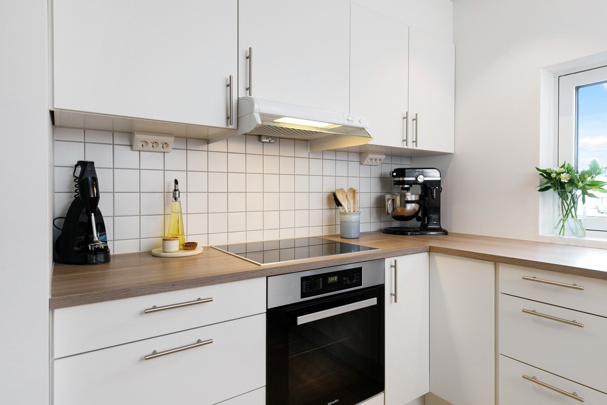 Kjøkkenet har hvit og stilren innredning fra Sigdal, benkeplater i laminat og fliser på vegg under overskapene. Galleribilde