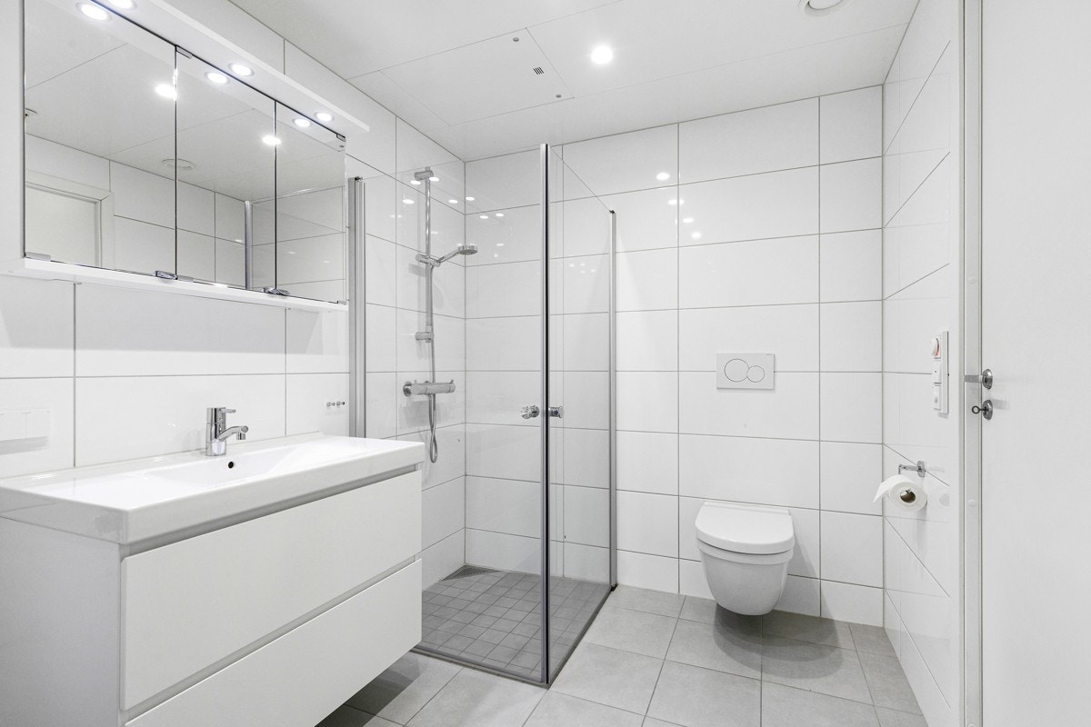 Leiligheten har wc-rom og bad, og begge har grå gulvfliser, hvite veggfliser, varmekabler, downlights og vegghengt toalett. Galleribilde
