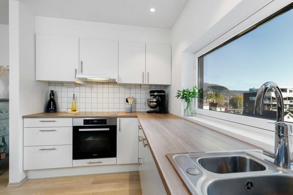 Det er downlights i tak og godt lysinnslipp fra et stort vindu over kjøkkenbenken med oppvaskkum. Galleribilde