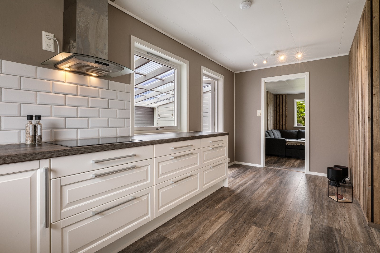 Vegg over benkeplate er belagt med hvite fliser. Overskap, vitrineskap og vinhylle. Galleribilde