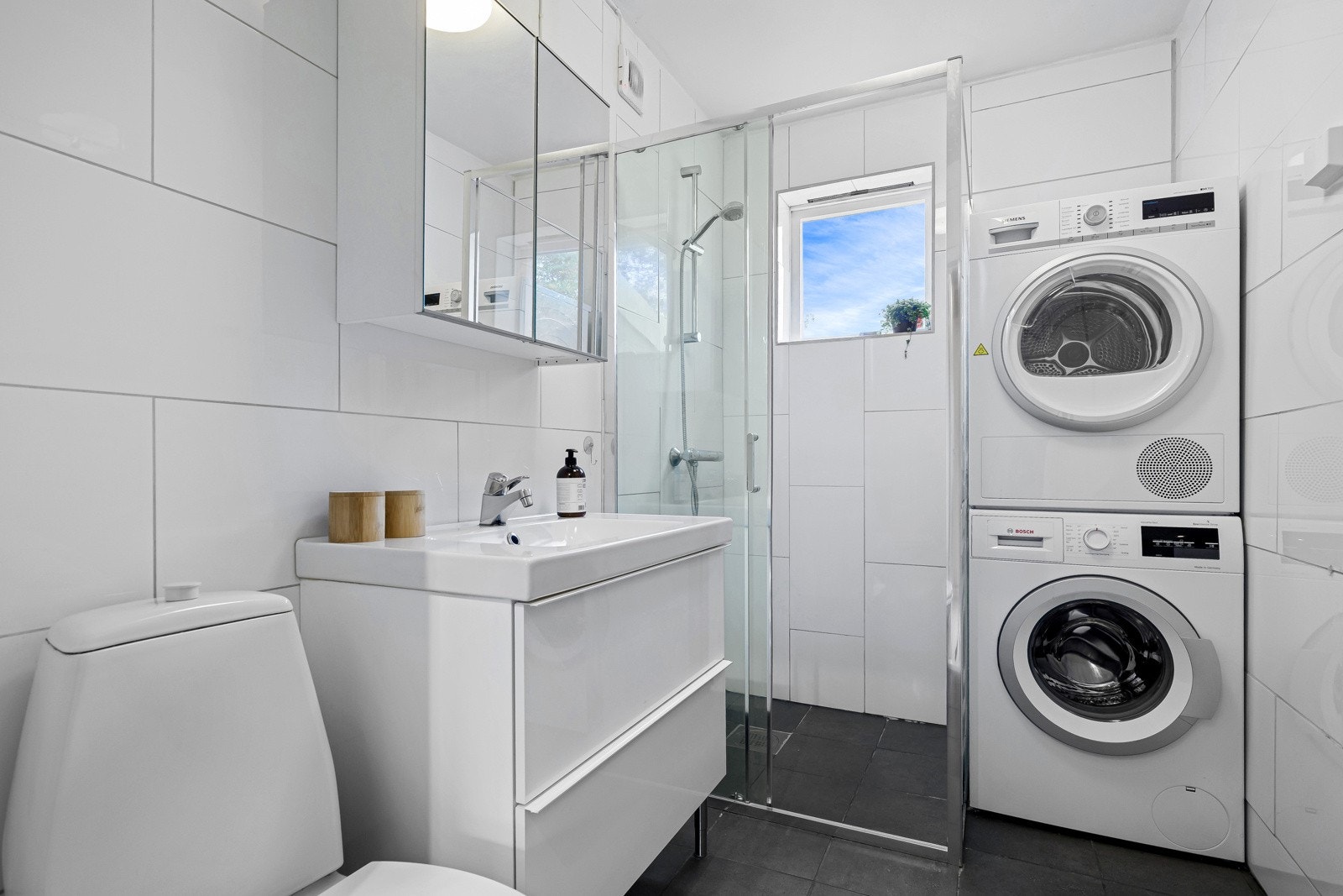 Baderommet inneholder dusj med fast felt, benkeskap, servant, veggskap med speilfronter og toalett. Opplegg for vaskemaskin og tørketrommel. Galleribilde