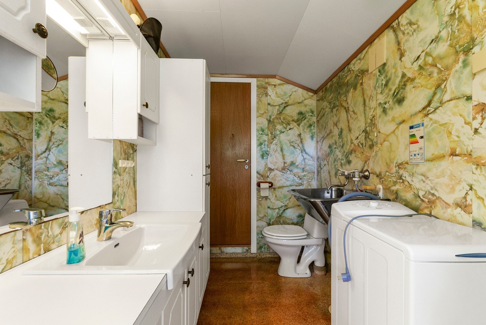 Fra kjøkkenet er det inngang til badet, som var nytt i 1985. Badet er innredet med servant med over- og underskap, veggspeil, høyskap, vegghengt utslagsvask i stål, frittstående toalett og dusjhjørne med dusjdører med fast sokkel mot gulv. Galleribilde