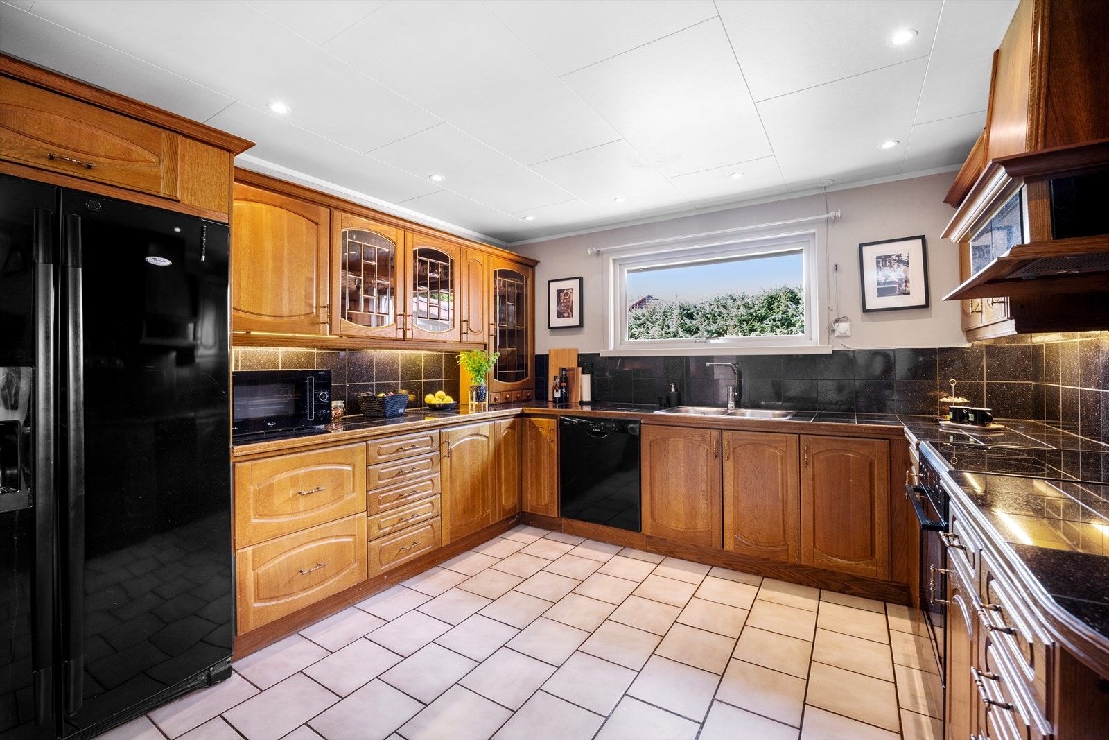 Kjøkkenet er innredet med profilerte fronter i eik, flislagte benkeplater med nedfelt oppvaskkum, fliser mellom benk og overskap, og ventilator Galleribilde