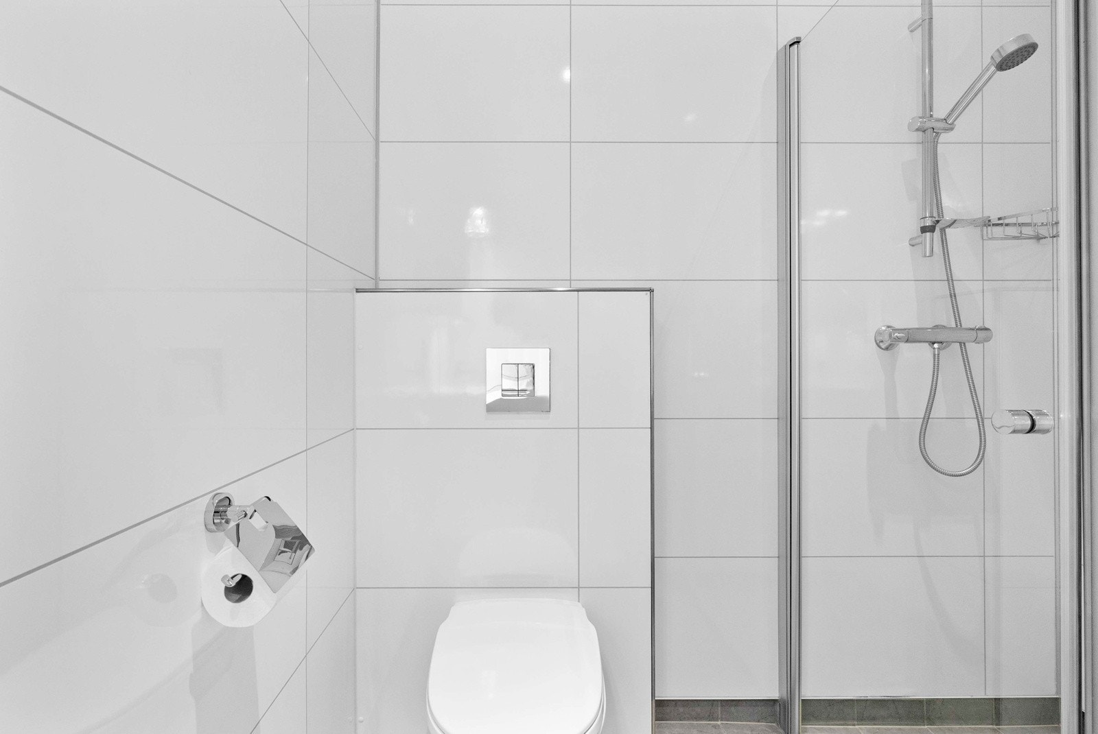 Badet er innredet med servant med underskap, speilskap, veggmontert dusj i nisje med glassdør samt vegghengt toalett. Galleribilde