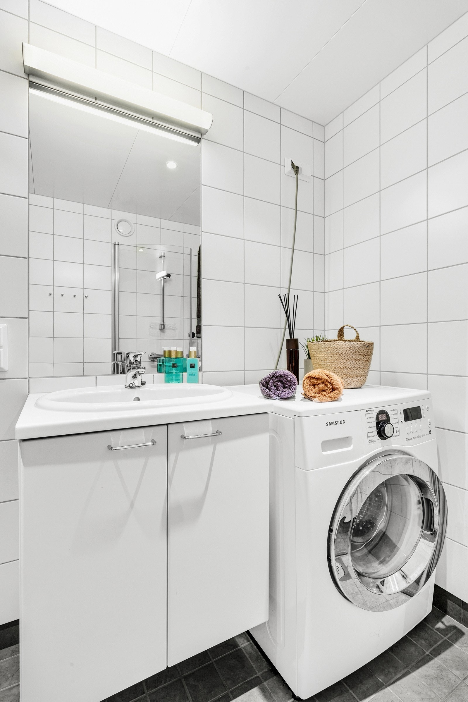 Baderommet består av flislagte overflater, svingbare dusjdører, vegg hengt toalett, servantskap og innfelt speil samt opplegg for vaskemaskin. Galleribilde