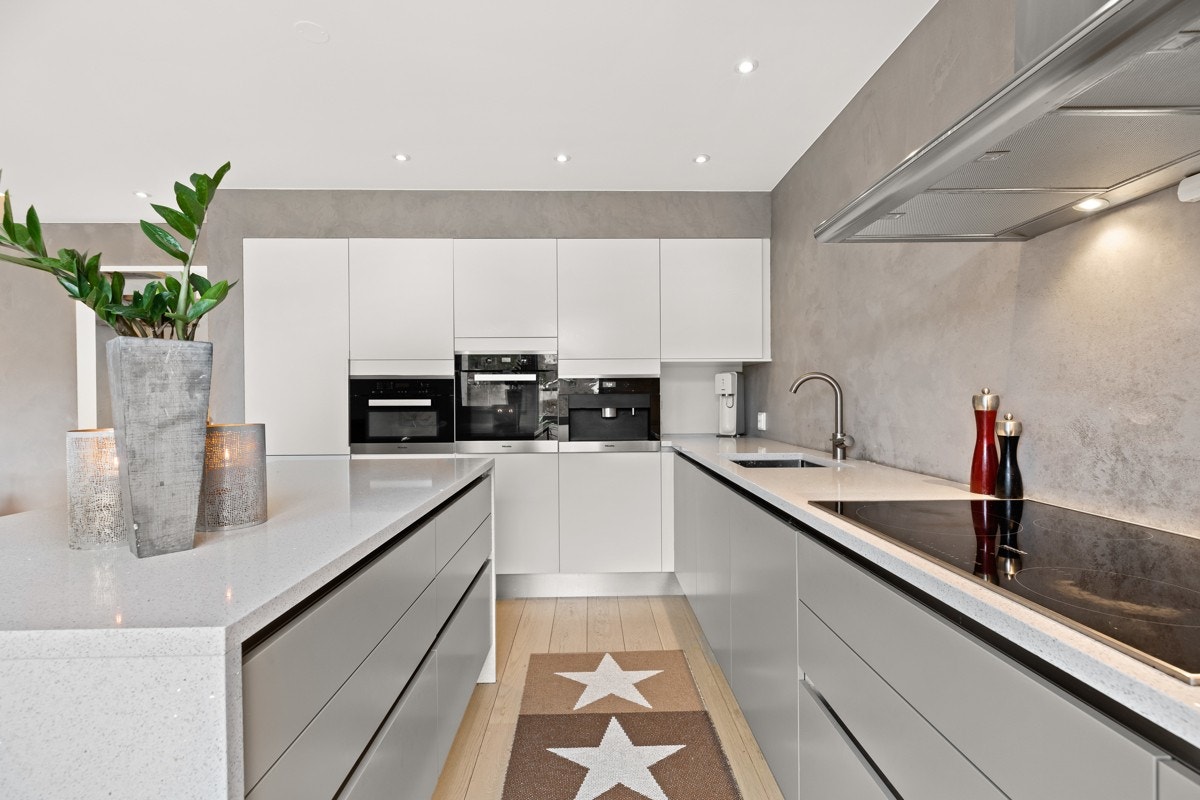 Moderne kjøkkeninnredning med hvite fronter, benkeplate av stein og nedfelt stålkum. Galleribilde