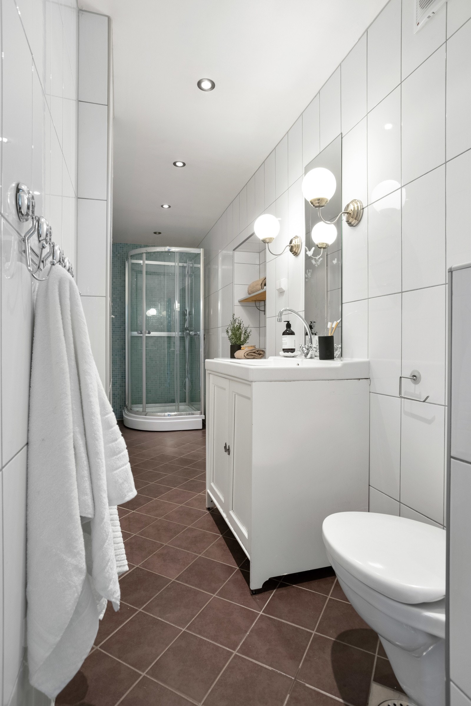 Badet er utstyrt med gulvstående servantskap med hvite profilerte fronter og keramisk vask med to-greps armatur i krom, skap med hyller tilpasset nisje og eletrisk håndkletørker Galleribilde