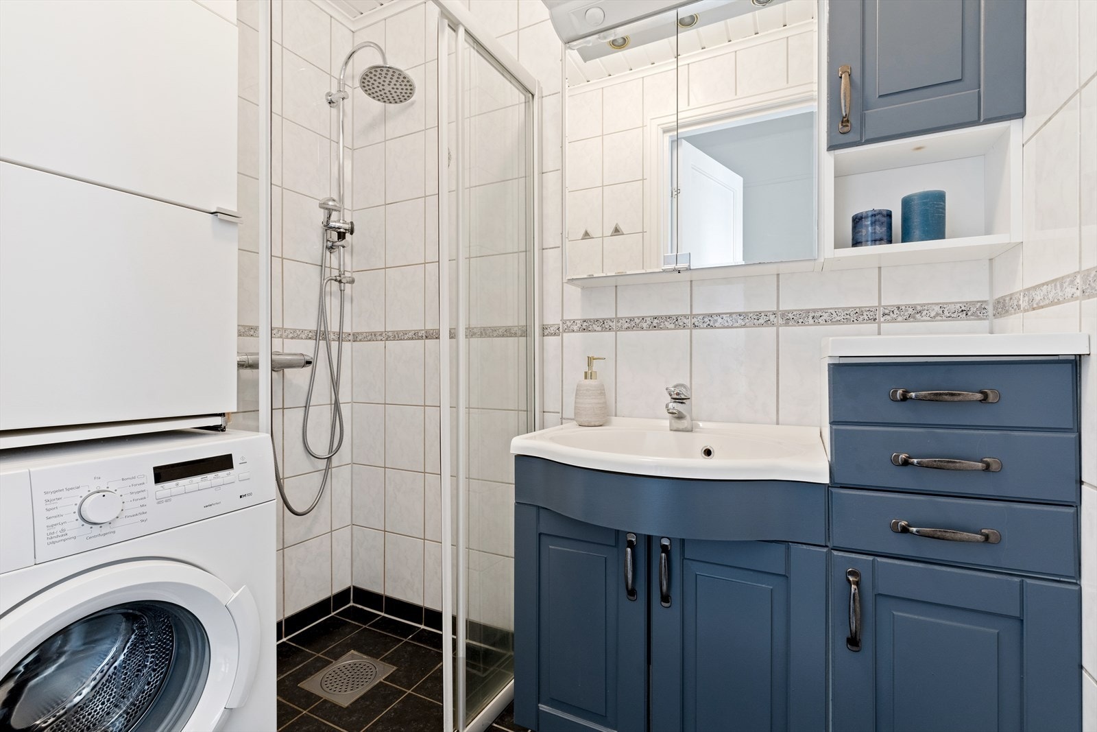 Flislagt bad/vaskerom med lyse fliser på vegg og mørke fliser på gulv. Servantmøblement med flere skap,
over servanten er det et stort speil med integrert belysning. Videre har badet dusjhjørne, samt opplegg for
vaskemaskin og varmekabler i gulv. Galleribilde