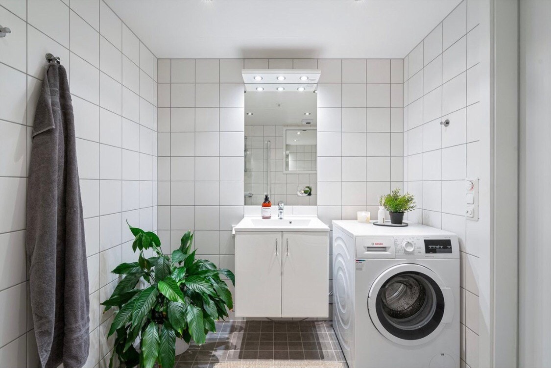 Pent, flislagt bad med enkel servant innredning, speil med overbelysning og opplegg for vaskemaskin. Galleribilde