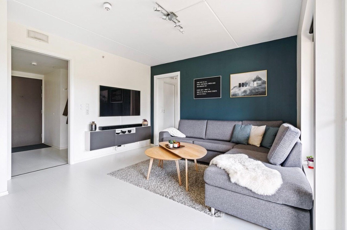 Stuen er pent innredet med hvit 1-stavs laminatgulv, og lyse veggflater med en moderne kontrastvegg i en grønn fargetone. Galleribilde