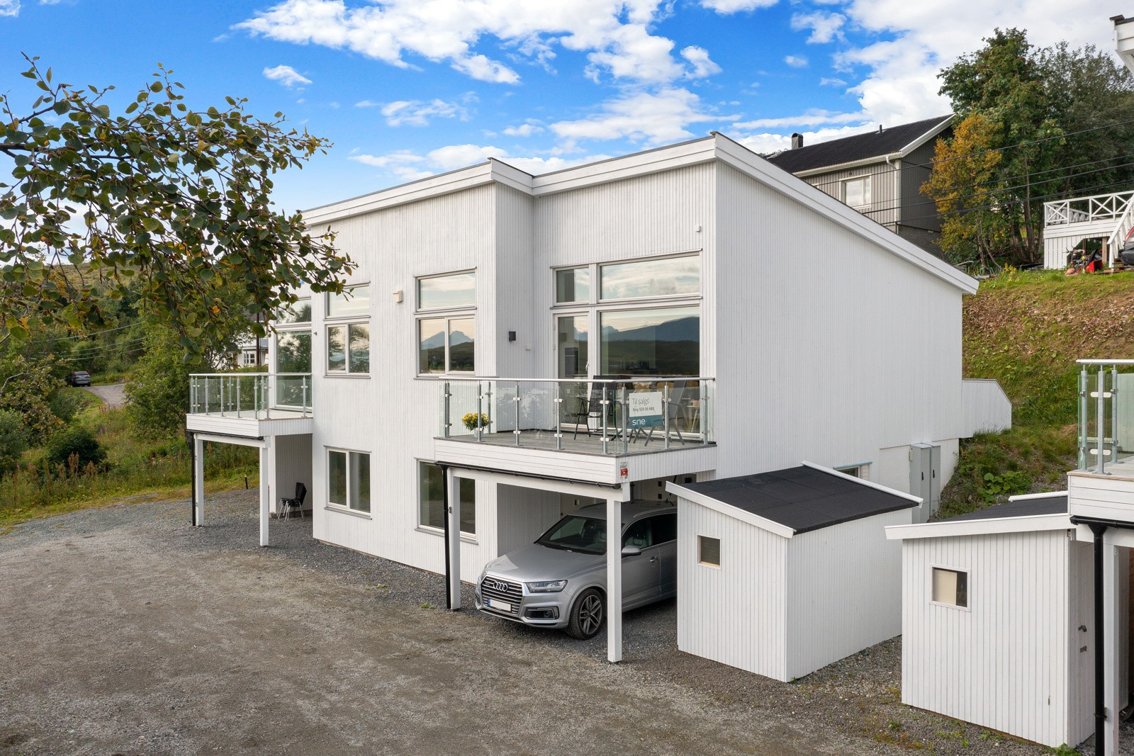 Fasade. Boligen har carport ved inngangsparti. Ved siden av carporten er det etablert en sportsbod.