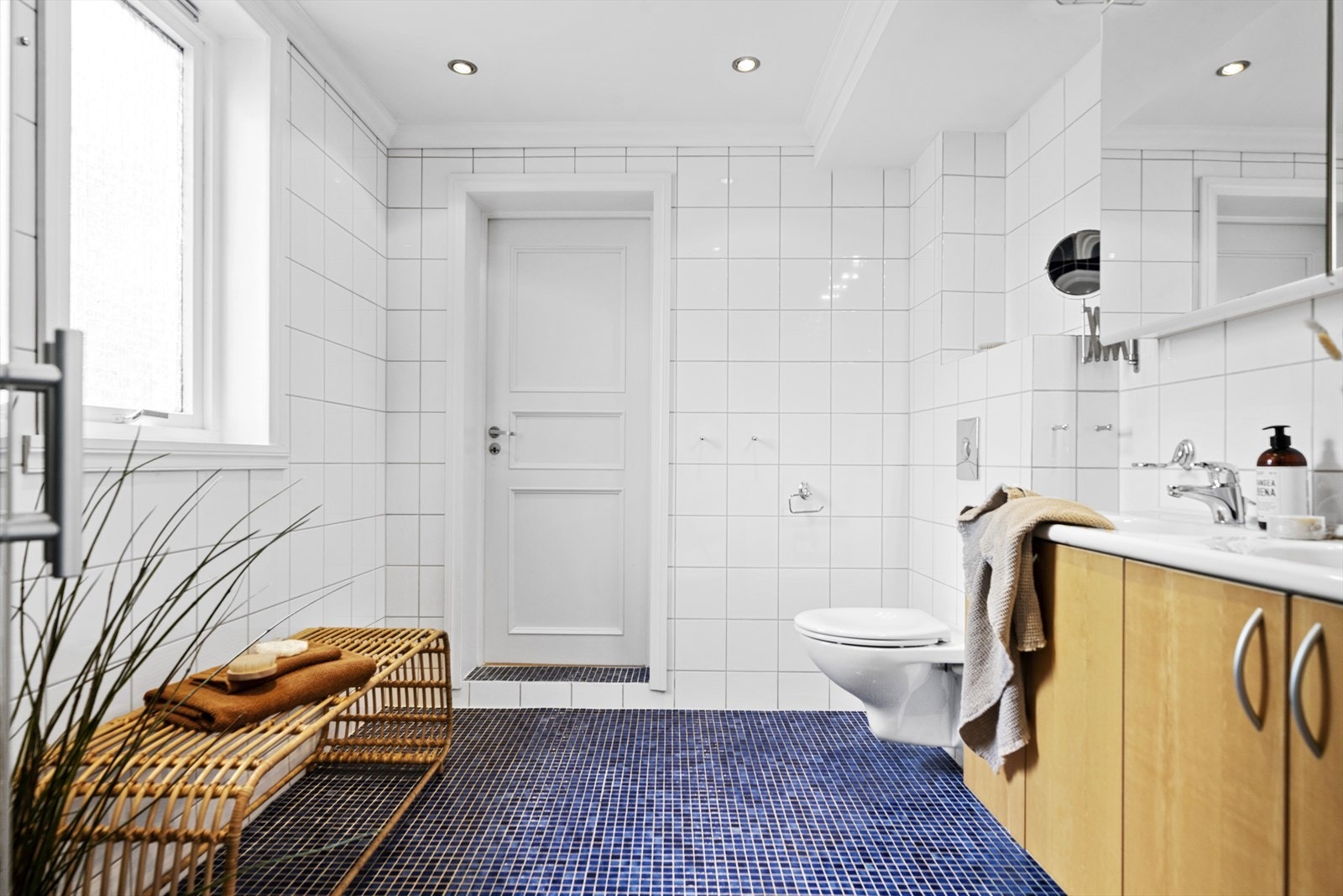 Pent bad med blå mosaikkfliser på gulv og tidløse hvite fliser på veggene med mørk blå fliser i dusjsonen. Galleribilde