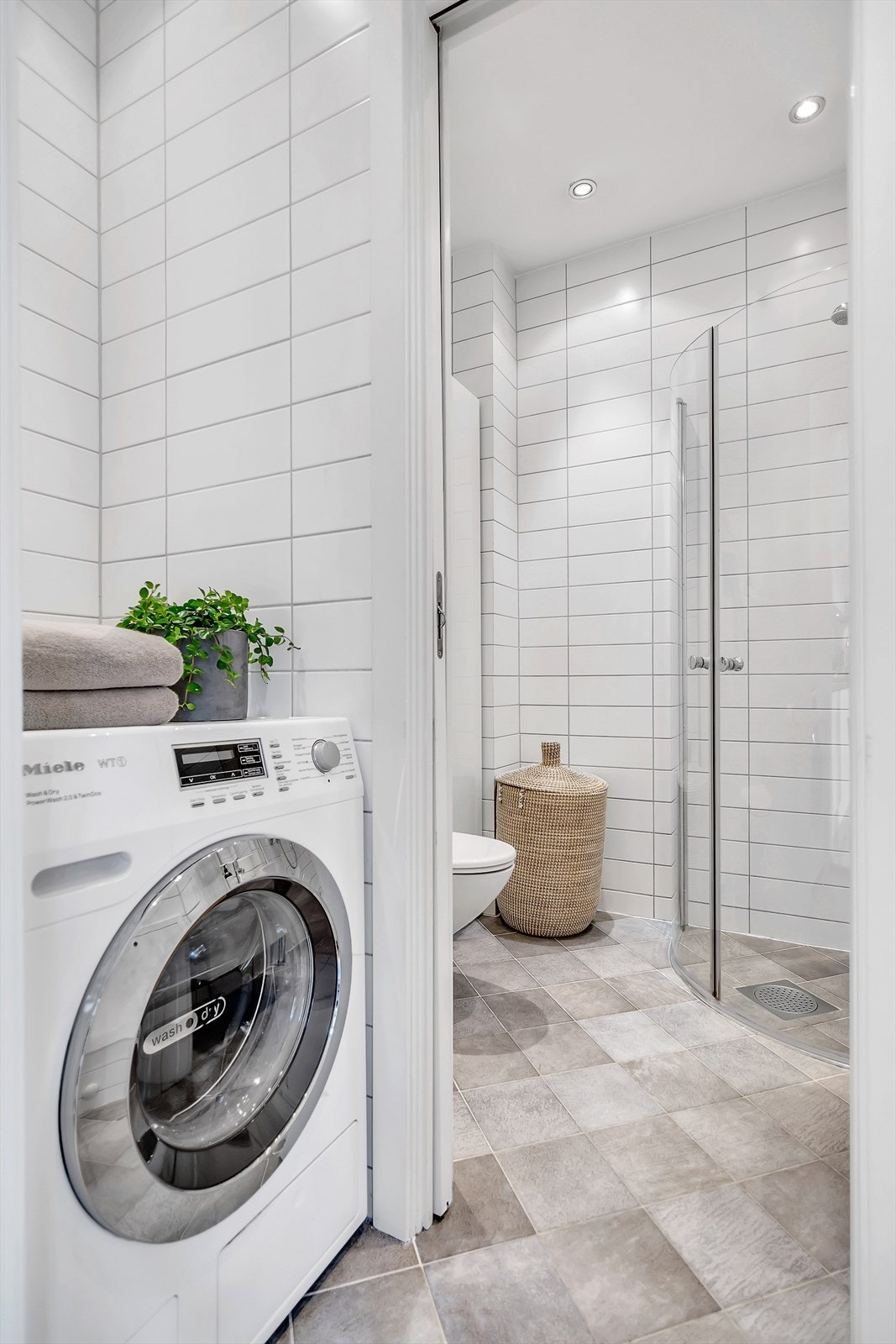 Delikat flislagt bad med opplegg for vaskemaskin, vegghengt wc, servantskap med speil og dusjhjørne med innfellbare glassdører. Galleribilde