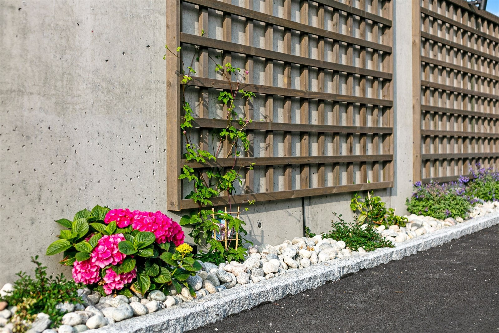 Felles uteområdet med postkassevegg og blomsterbed med nedgravd vanningssystem, i tillegg til avfallshus som er en estetisk detalj i seg selv. Galleribilde