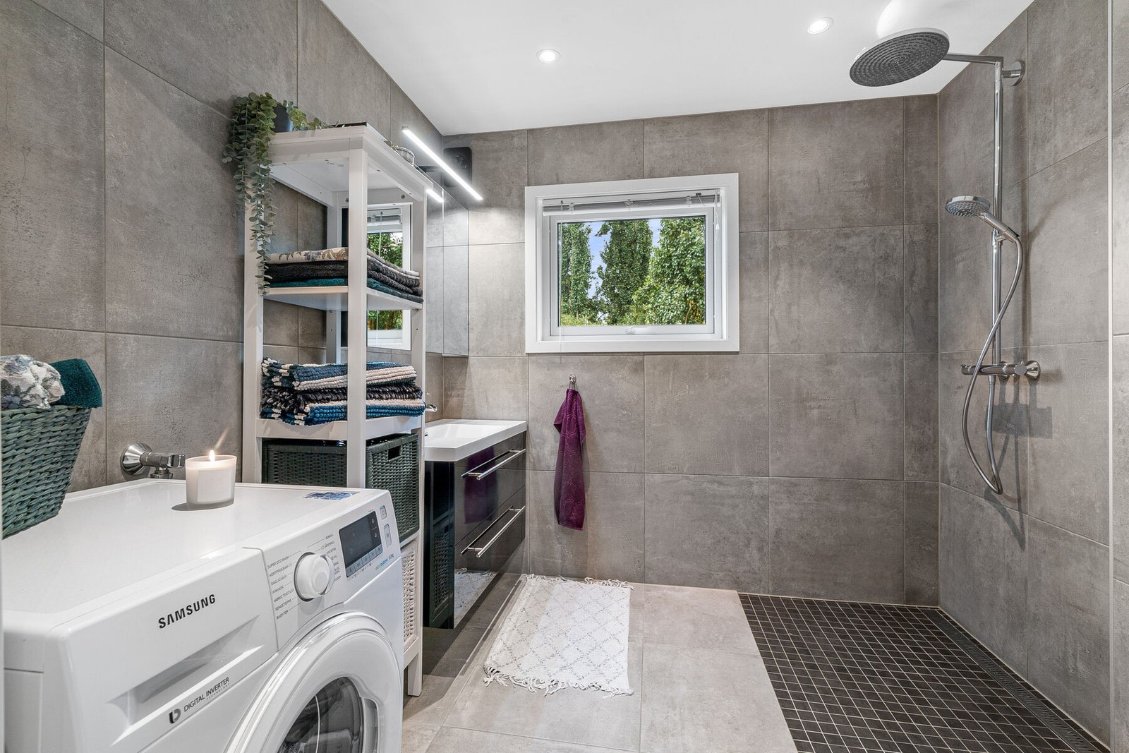 Nydelig bad fra 2018 med kvalitetsbevisste løsninger innredet med åpen dusjplass med dusjgarnityr montert på vegg, veggmontert WC, kran og avløp for vaskemaskin, rørskap, servantplate med underskap og speilskap. Galleribilde