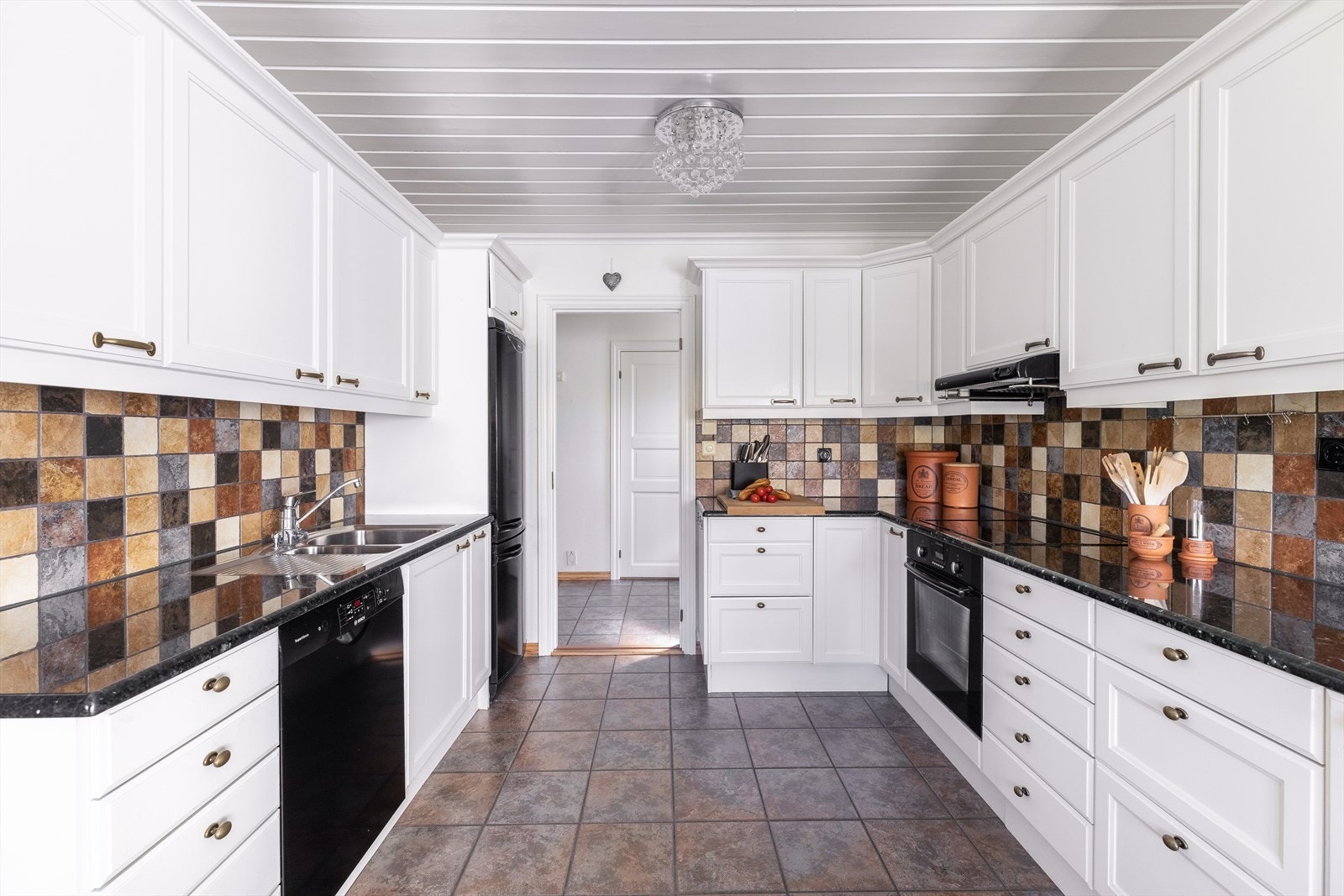 Videre er kjøkkenet utstyrt med integrert oppvaskmaskin, nedfelt stålvask med liten skyllekum med fliser over benkeplate, og belysning under overskap Galleribilde