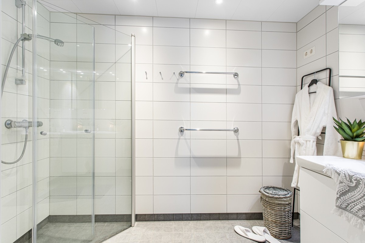 Delikat hovedbad med flotte fliser på gulv og vegger. Tidsriktig dusjplass med innsvingbare dusjvegger av glass, vegghengt wc, servant med over- og underskap hvorav overskap med speilfronter. Galleribilde