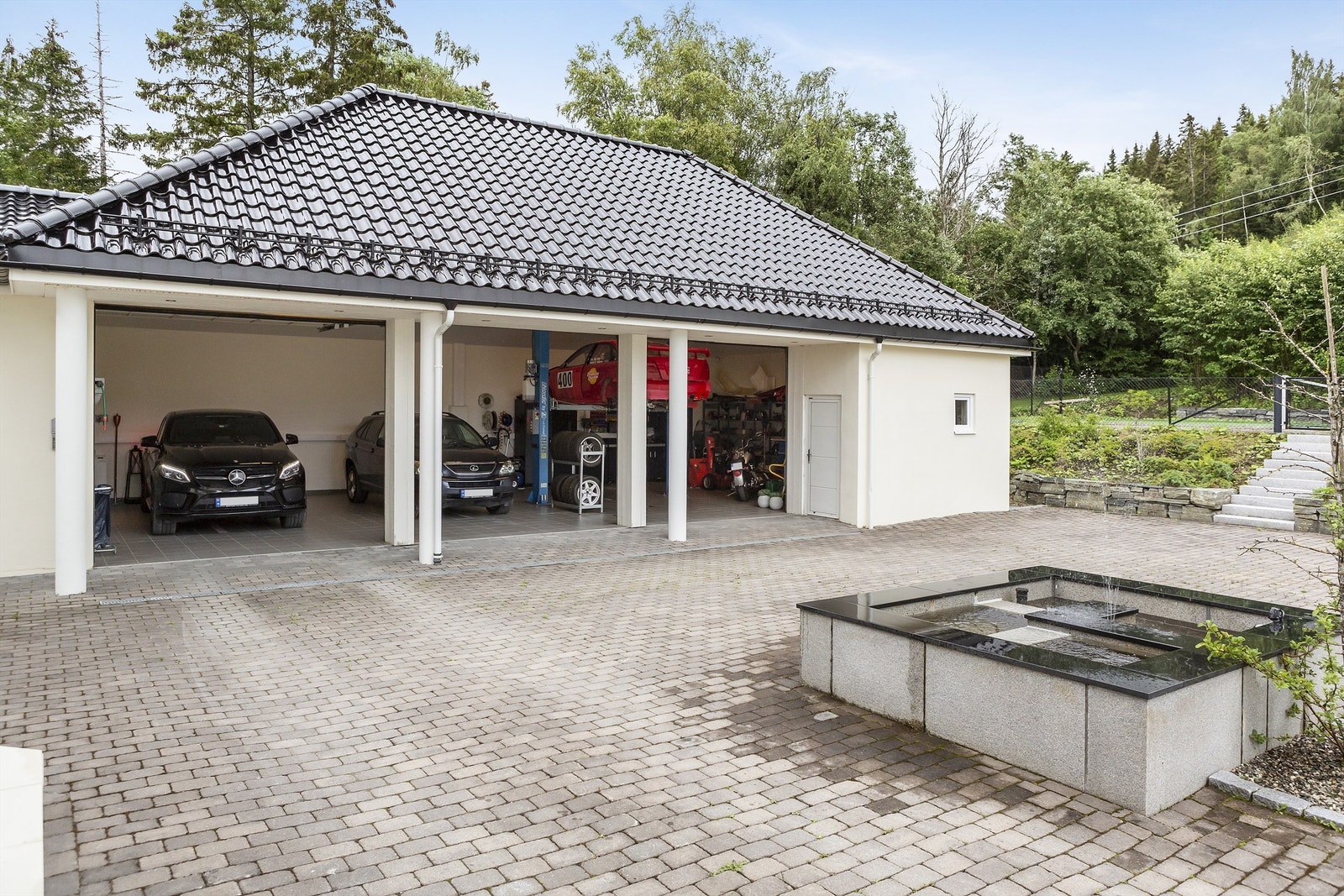 Eiendommen har trippelgarasje og stor, steinsatt gårdsplass med adkomst via en pent anlagt allé. Galleribilde