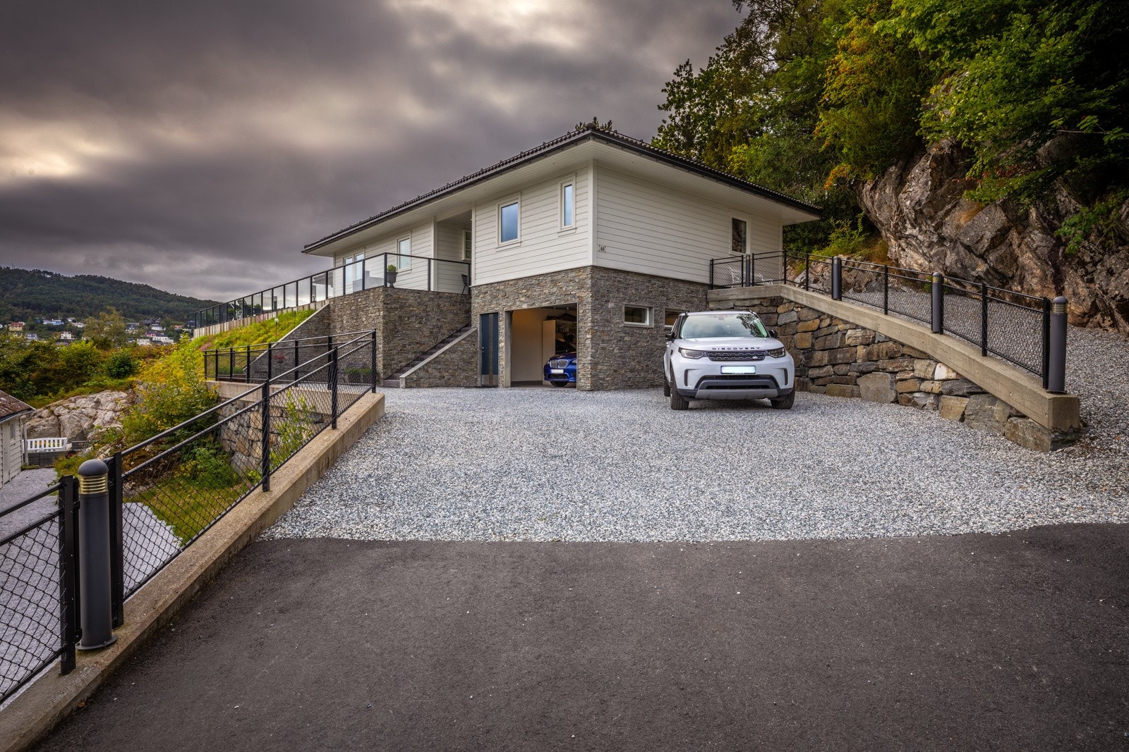 Meget innbydende inngangsparti med asfaltert innkjørsel, gruset parkering, natursteinmurer og utebelysning. Galleribilde