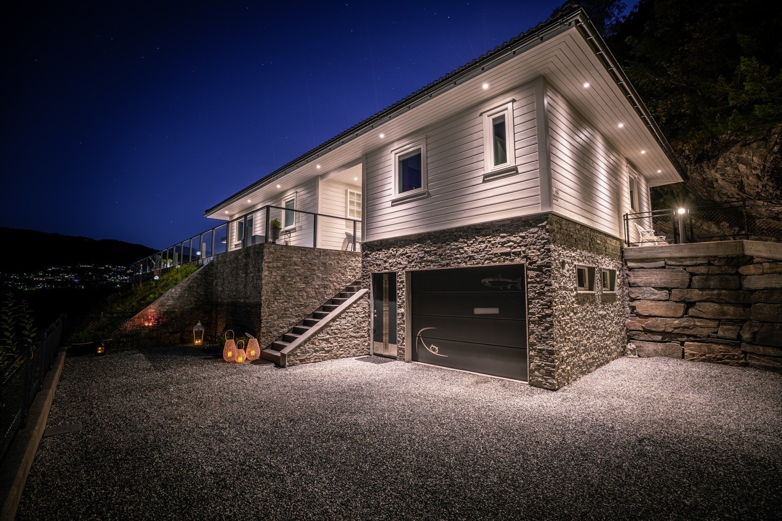 Kveldsfoto av fasade. Boligen har integrert garasje med bod i bakre del på 9 kvm. Det er også flere biloppstillingsplasser på tomten. Galleribilde