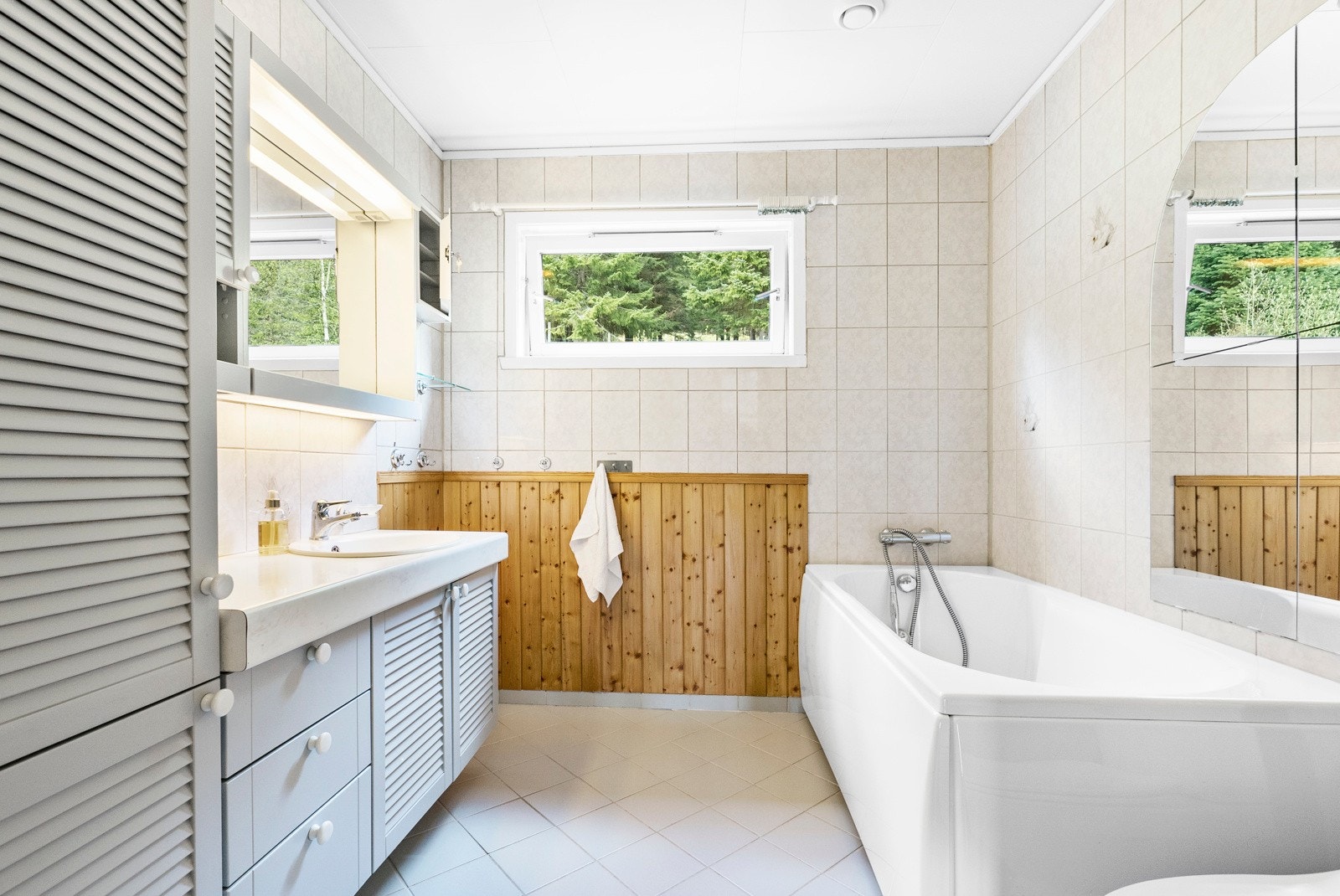 Dette er badet i 1. etasje. Rommet er innredet med servant med over- og underskap, høyskap, veggspeil med lyspunkt, badekar og frittstående toalett. Varme i gulvet. Galleribilde