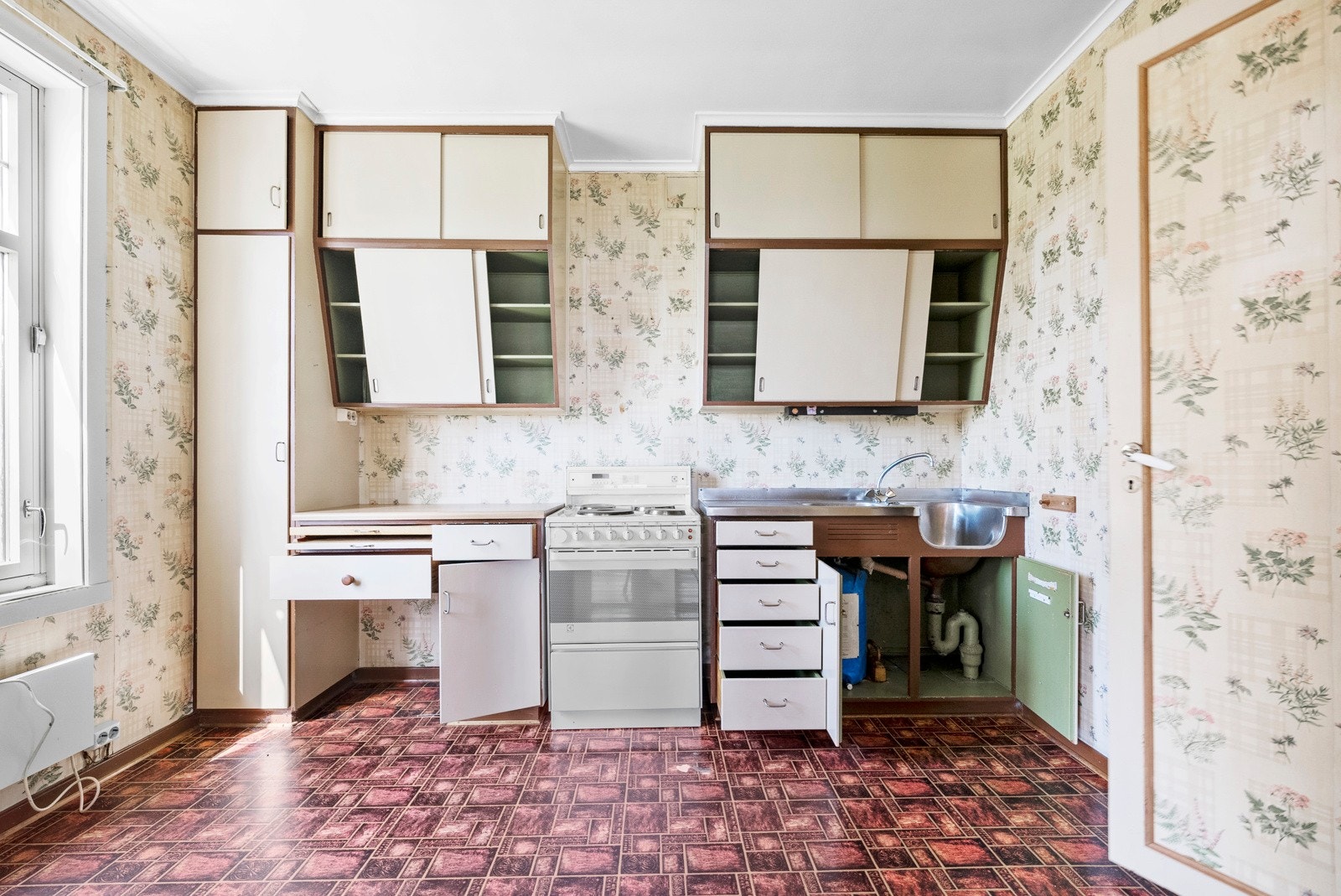 Dette er kjøkkenet med tilgang fra gangen. Eldre kjøkkeninnredning med høyskap, over- og underskap med fronter av trefiberpanel. Benkeplate av laminat. Vask med to kummer og større sidefelt i stål. Galleribilde