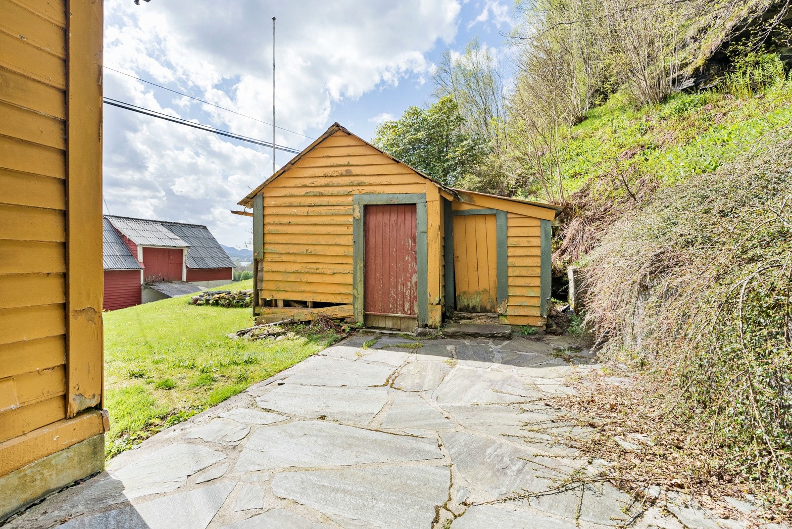 Inngangspartiet er pent opparbeidet med plen og skiferheller. Enkel tilgang til uthuset. Galleribilde