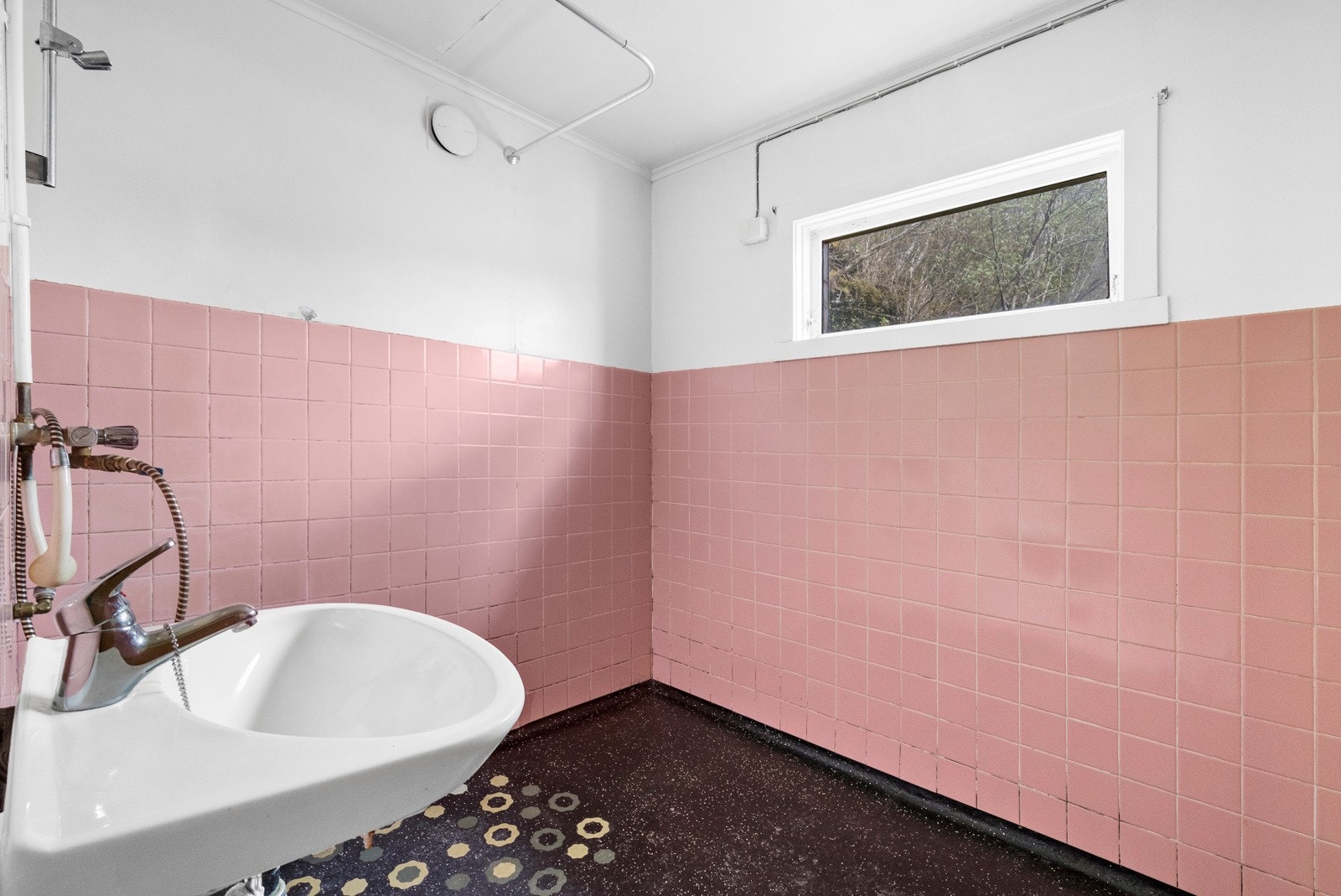 Eldre bad med epoxy på gulv og fliser på vegg i brystningshøyde med malte trefiberplater over. Vegghengt vask med lyspunkt over. Dusjhjørne med blandebatteri og oppheng for handdusj montert på vegg. Galleribilde