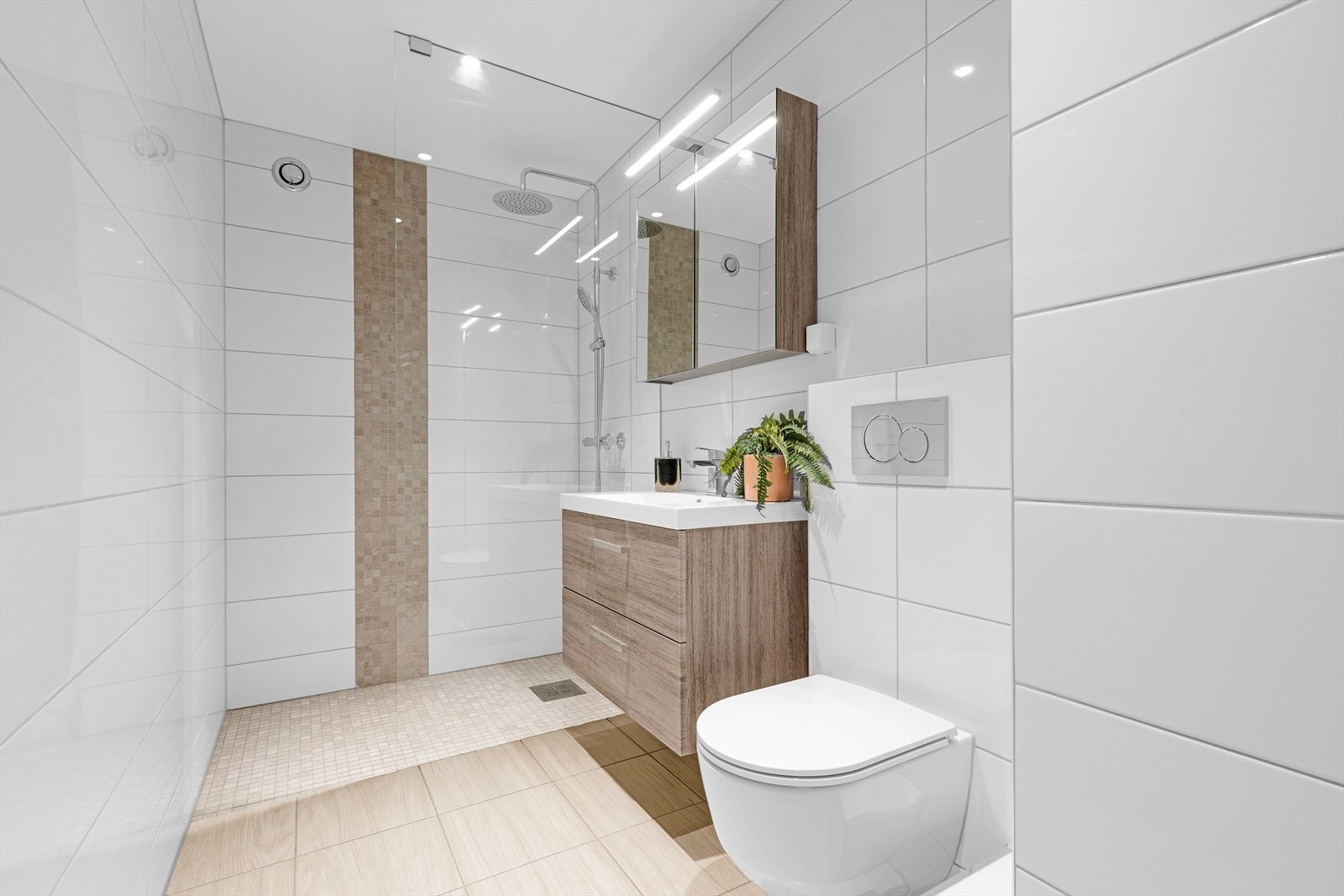 Baderomsinnredning bestående av benkeskap med glatte fronter. Veggskap med speilfronter og belysning over servant. Dusj med fast felt i herdet glass, servant i helstøpt plate og veggfestet klosett med innebygget
sisterne Galleribilde