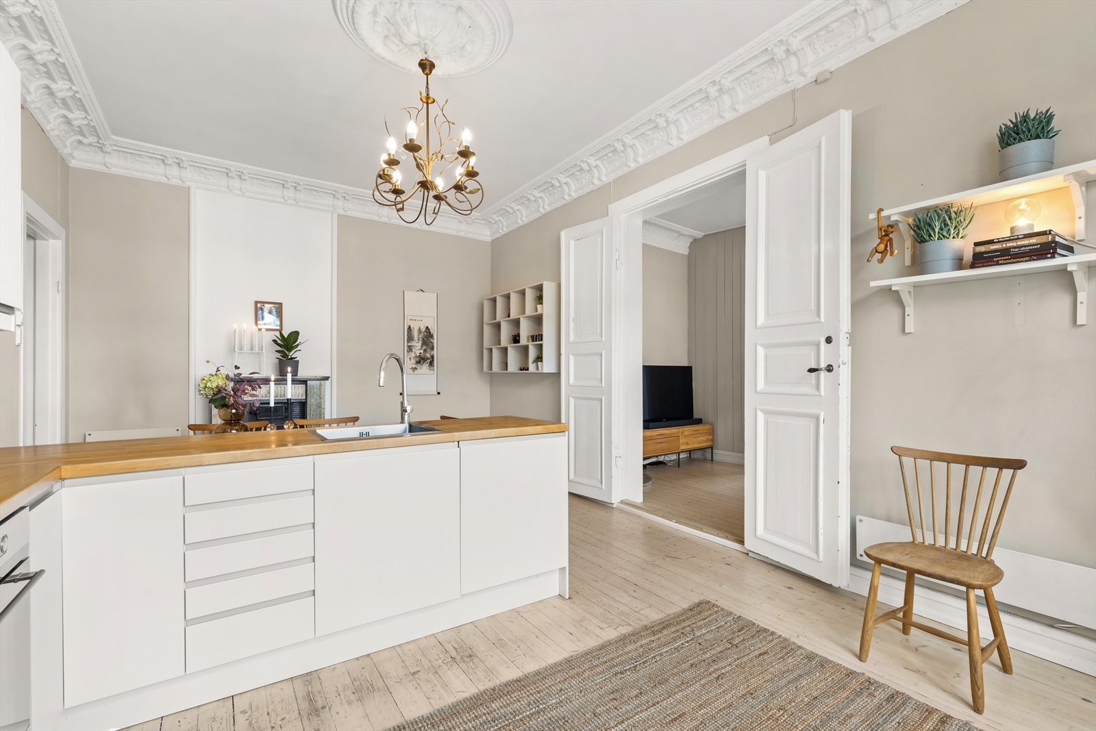 Kjøkkeninnredningen har hvite slette lakkerte skapfronter, heltre benkeplate med glassplate på bakvegg, oppvaskkum, ventilator med kullfilter. Galleribilde