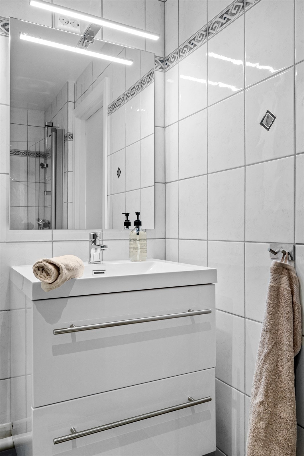 Stilren baderomsinnredning med servant og et ekstra skap til venstre for innredningen Galleribilde