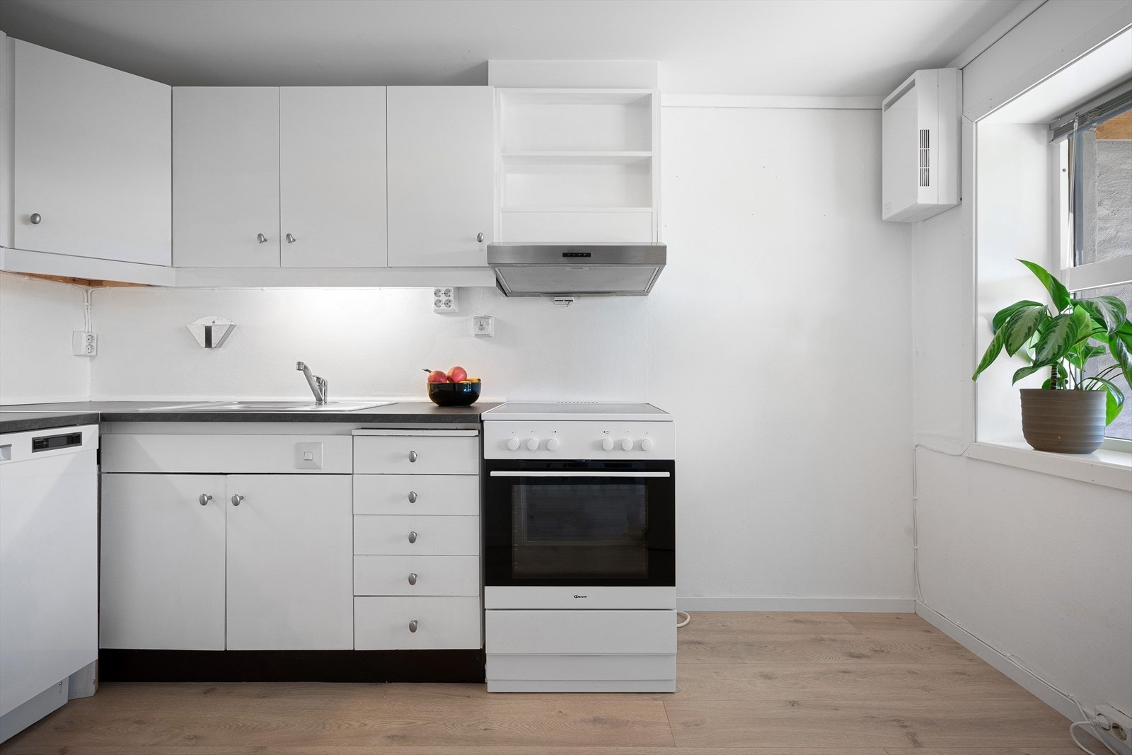 Kjøkkenet er romslig med hvit innredning og plass til komfyr og ventilator, oppvaskmaskin og benkekjøleskap Galleribilde
