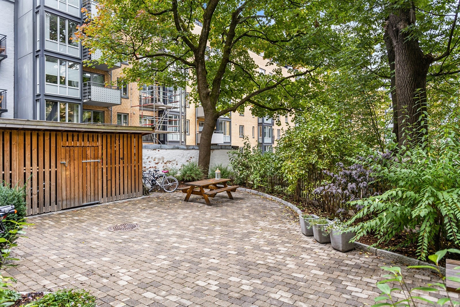 Pent opparbeidet bakgård med brostein, beplantning, sittegrupper og sykkelbod. Galleribilde