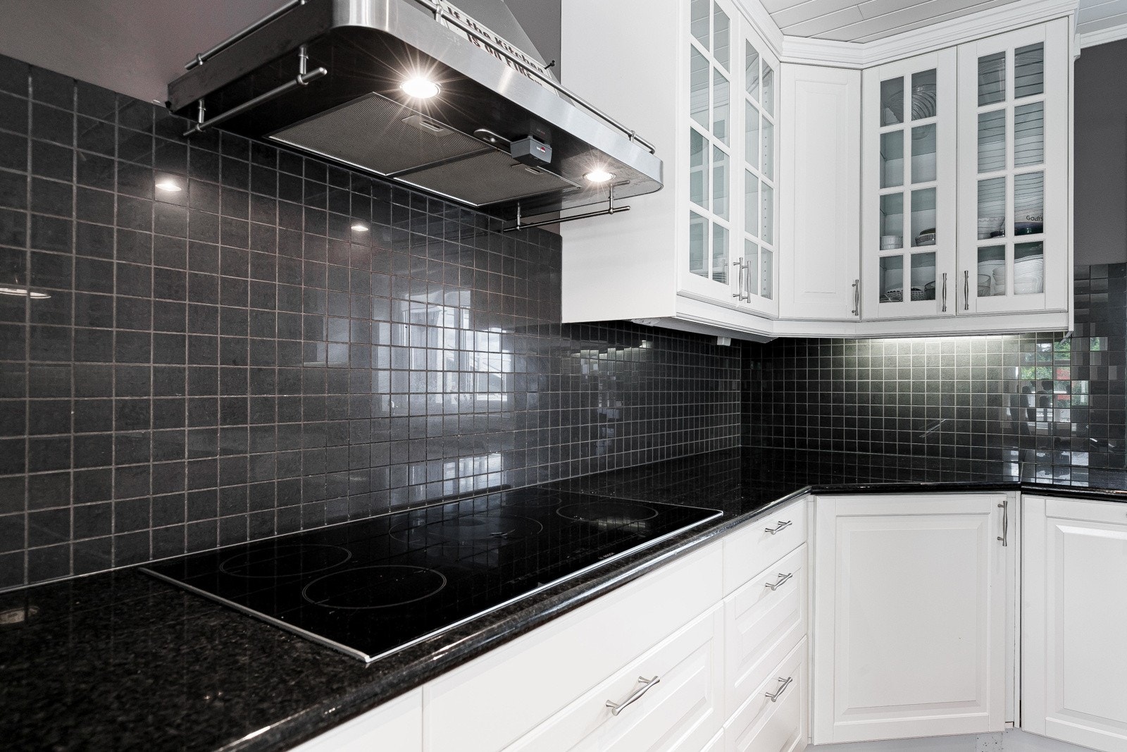 Over benken er det belysning og sorte mosaikkfliser, og over kokesonen er det montert en stilren ventilatorhette av stål. Galleribilde