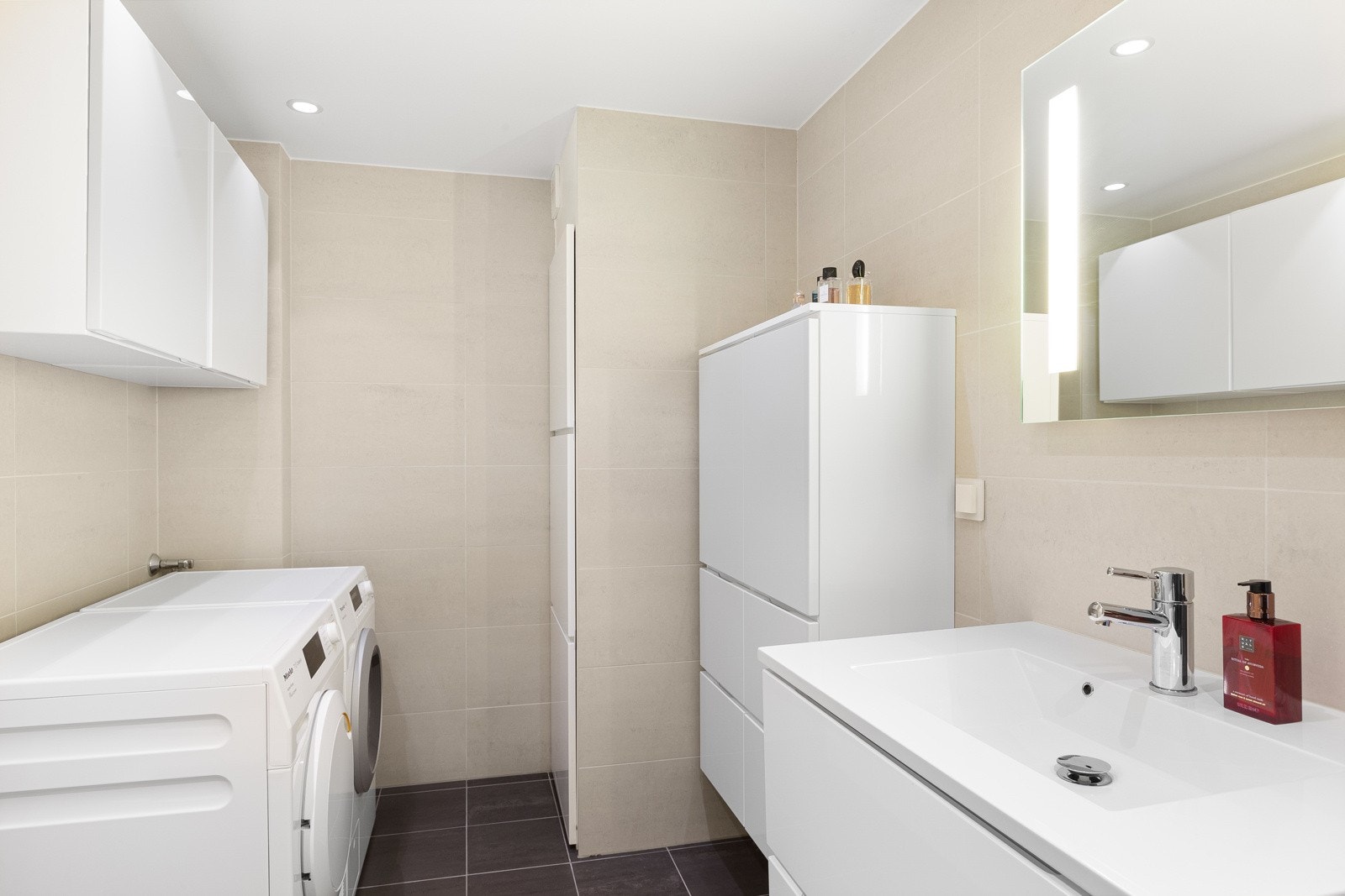 Badet har også fint opplegg for vaskemaskin og tørketrommel. Gode oppbevaringsløsninger i flere skap og fint speil med belysning. Galleribilde