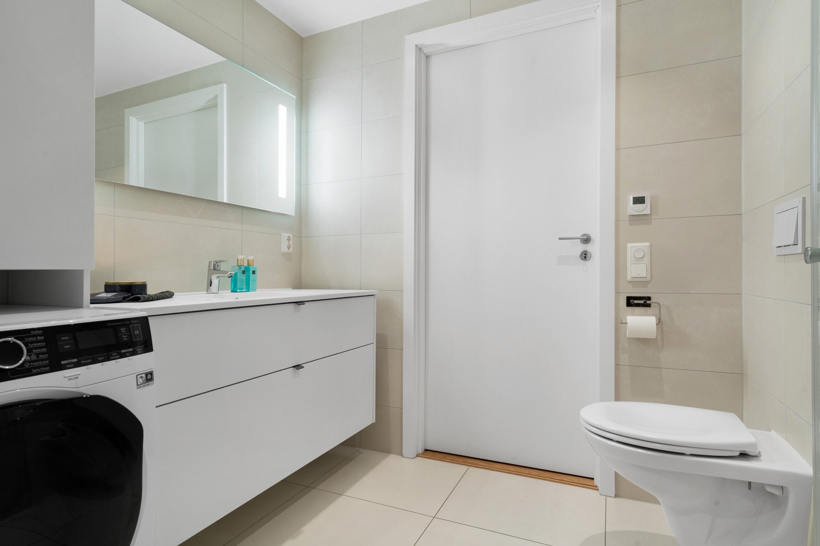 Moderne baderom med vegghengt toalett, baderommsinnredning, dusjhjørne og opplegg for vaskemaskin Galleribilde