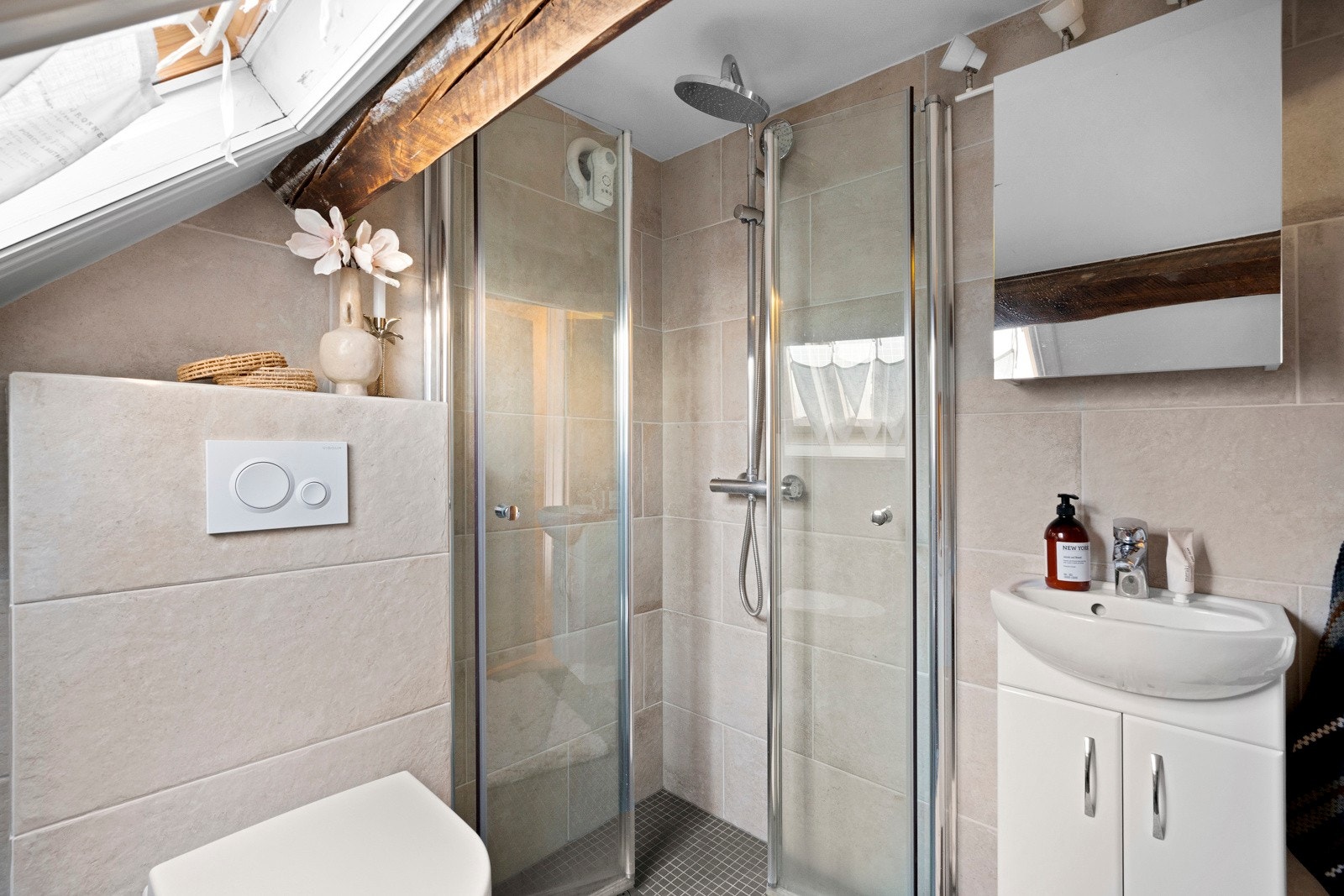 Badet har lys beige fliser på veggene, hvitmalt skråhimling og grå fliser på gulv med gulvvarme. Galleribilde