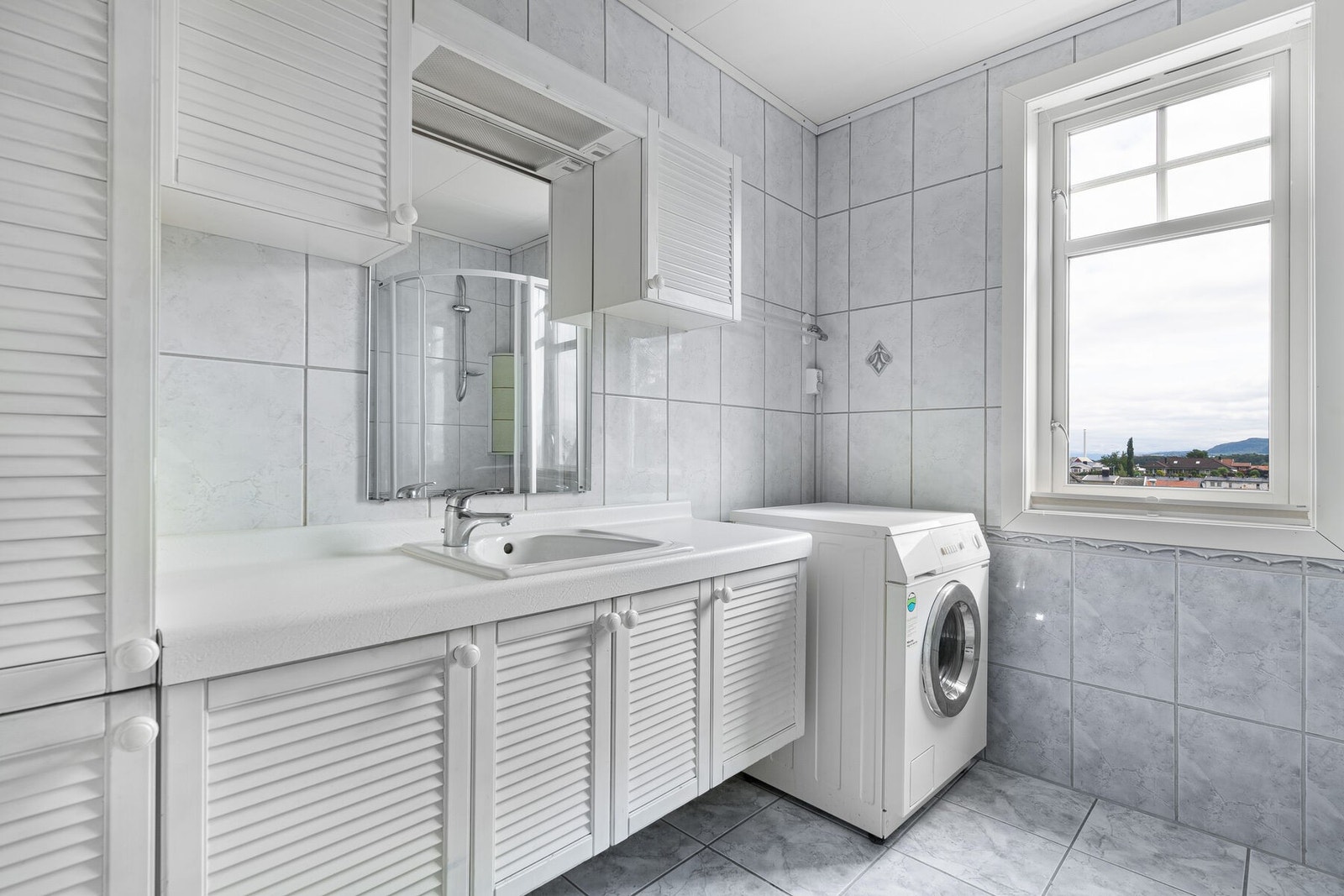 Flislagt bad med opplegg for vaskemaskin. Badet anbefales renovert av takstmann - bad/våtrom oppført med byggeforskrifter fra før 1997, får automatisk TG 3 pga alder uavhengig om det registreres avvik/slitasje. Galleribilde