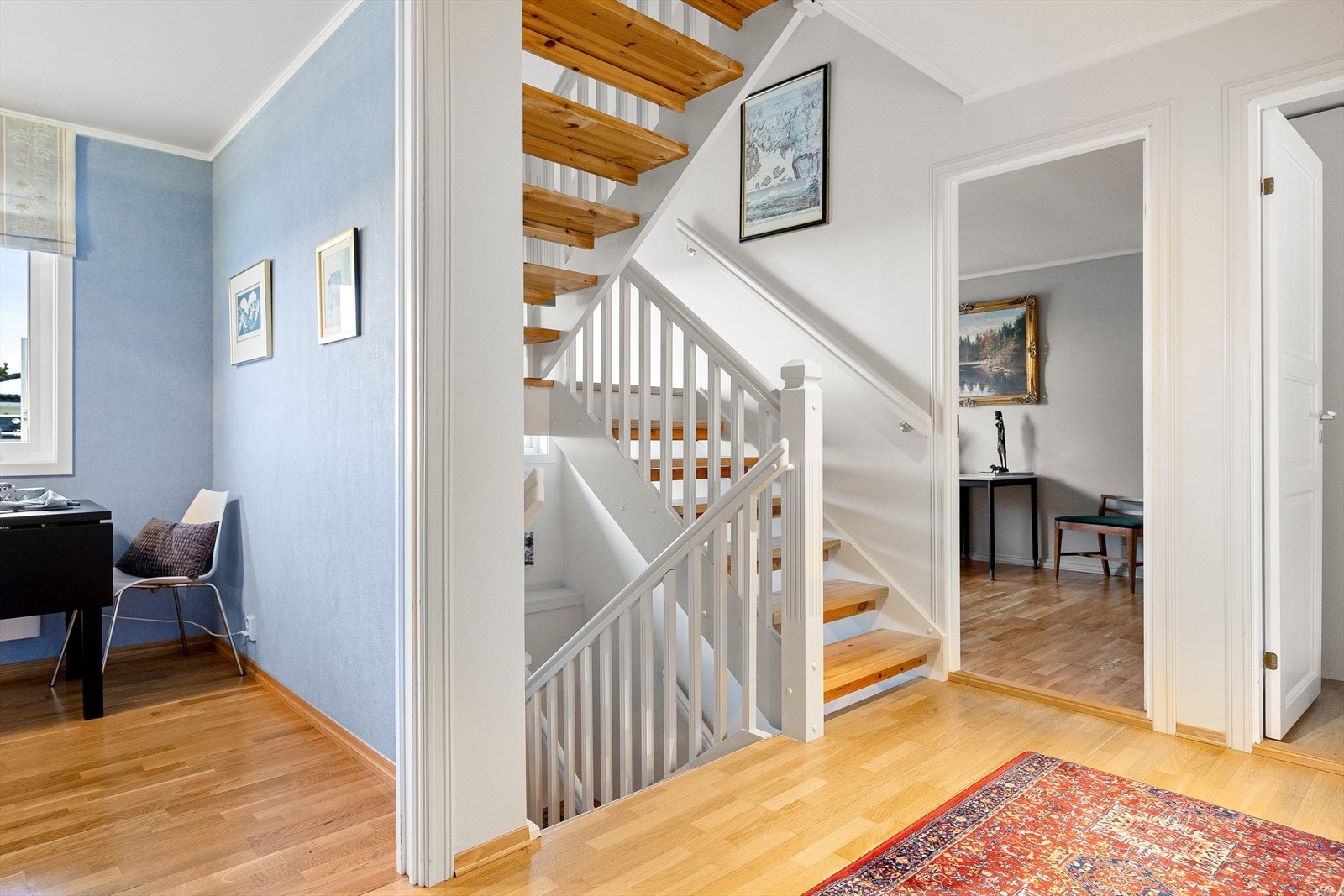 Rettvinklet trapp med trappetrinn og rekkverk av treverk. Du ser nå kjøkkenet på venstre side av trappen, og inngang til to soverom på den høyre siden. Galleribilde