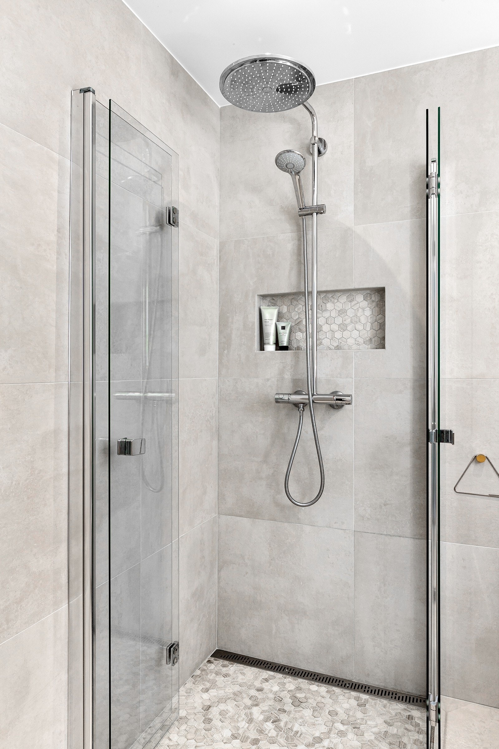 Stilren dusjnisje med slukrist, innfellbare glassdører, nisje i vegg til såpe og armatur med regnfalls- og hånddusj. Galleribilde